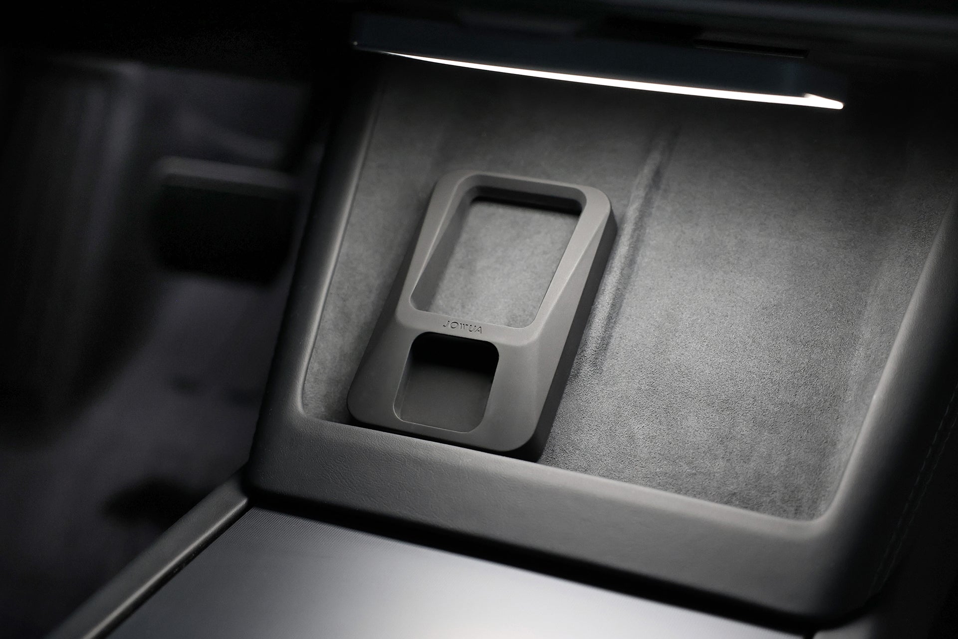 A JOWUA Power Dock Combo - Apple Accessory Charger for Tesla, in sleek black, sits on a soft felt-like surface under gentle light inside the car’s center console.
