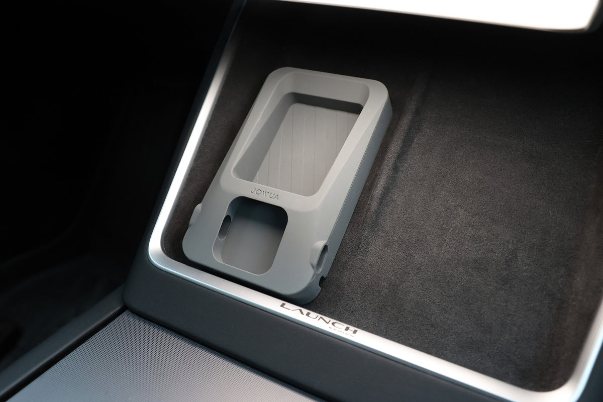 A gray JOWUA Power Dock Combo - Accessory Charger for Tesla is placed on a black surface with the word “LAUNCH” visible at the bottom edge, set within a sleek, modern vehicle interior featuring a Tesla wireless charging setup.