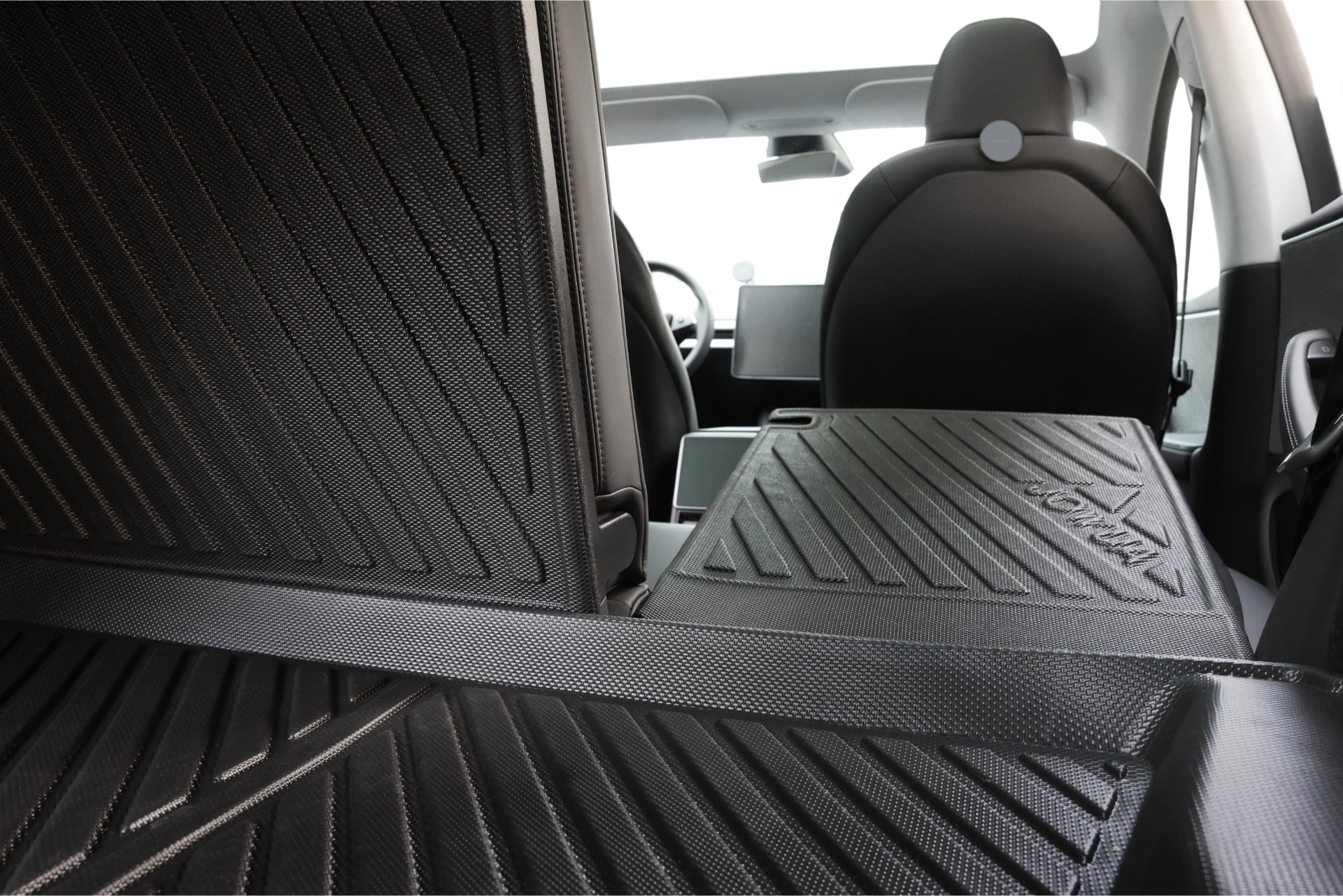 The interior of the Tesla Model 3 features foldable rear seats with a generous cargo area covered in protective, textured mats. Enhancing durability, the trunk liners are crafted from waterproof TPE material. In the background, you can see the driver and front passenger seats. The Model 3 All Weather Trunk Combo by JOWUA (Reengineered Model 3 Highland, 2024+) adds to this setup.