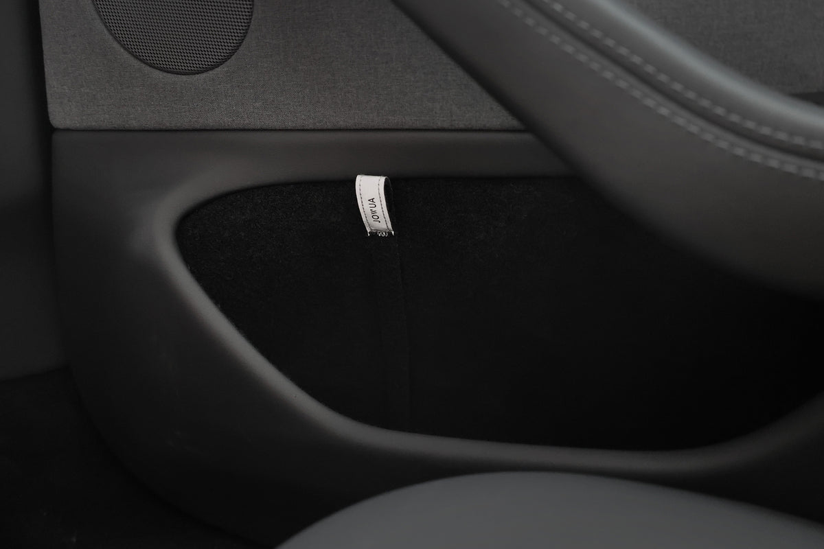Close-up of a JOWUA Reflective Rear Door Emergency Release Strap (Model 3 Highland, 2024+ / All Model Y) installed on a black car door panel, showing a fabric 