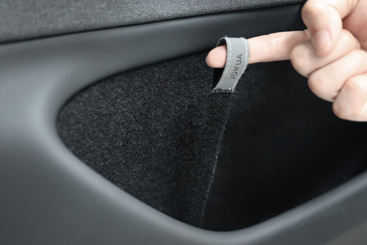 A hand pulls on a JOWUA Reflective Rear Door Emergency Release Strap, designed for Model 3 Highland (2024+) and all Model Y, shown attached inside a black car door pocket lined with dark felt-like material.