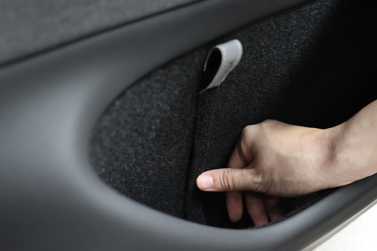 A hand pulls a JOWUA Reflective Rear Door Emergency Release Strap from a fabric-lined car door compartment—an essential accessory for safety and convenience in the Model 3 Highland (2024+) and all Model Y vehicles.