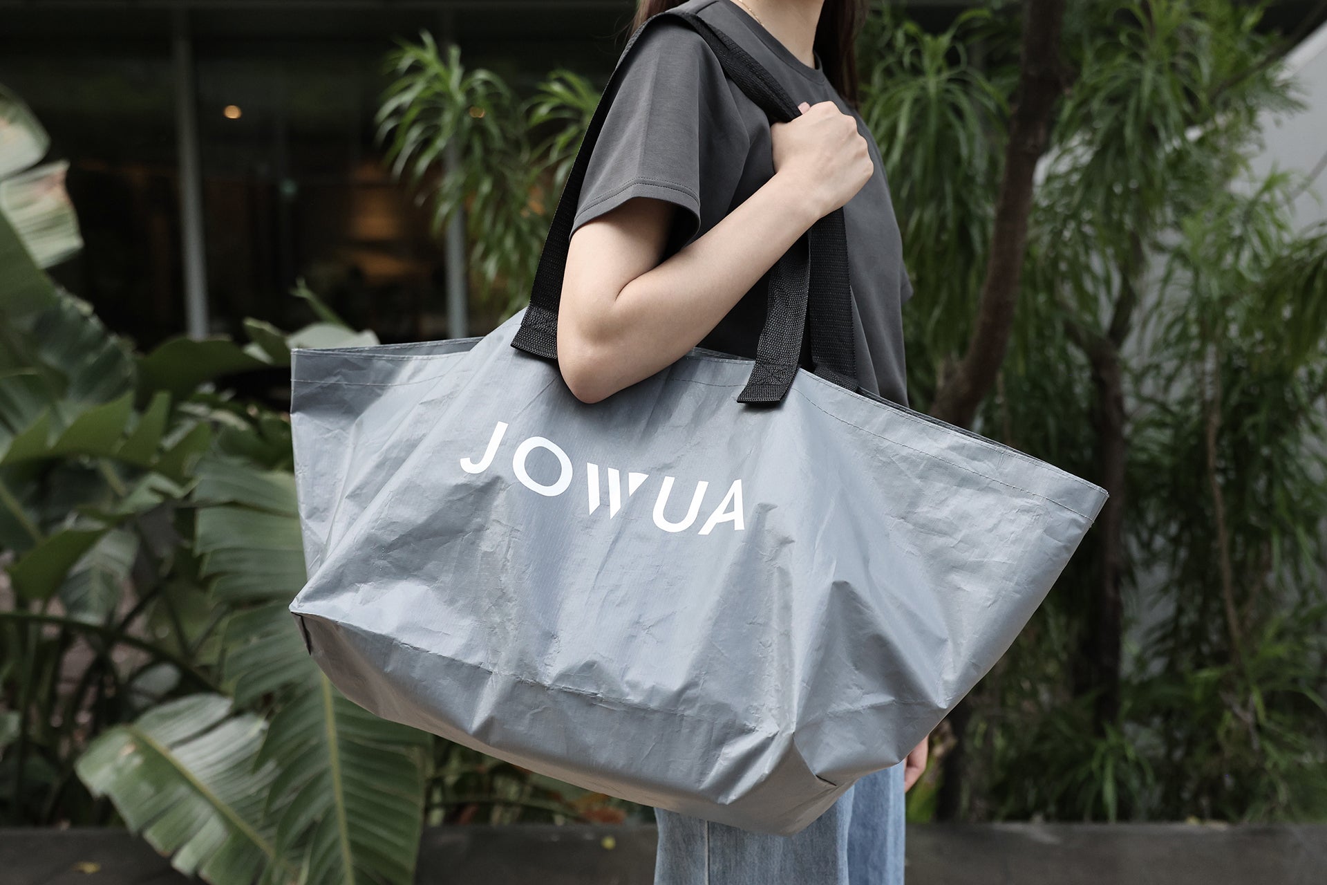 Outdoors, a person holds a large gray tote bag with black straps labeled 