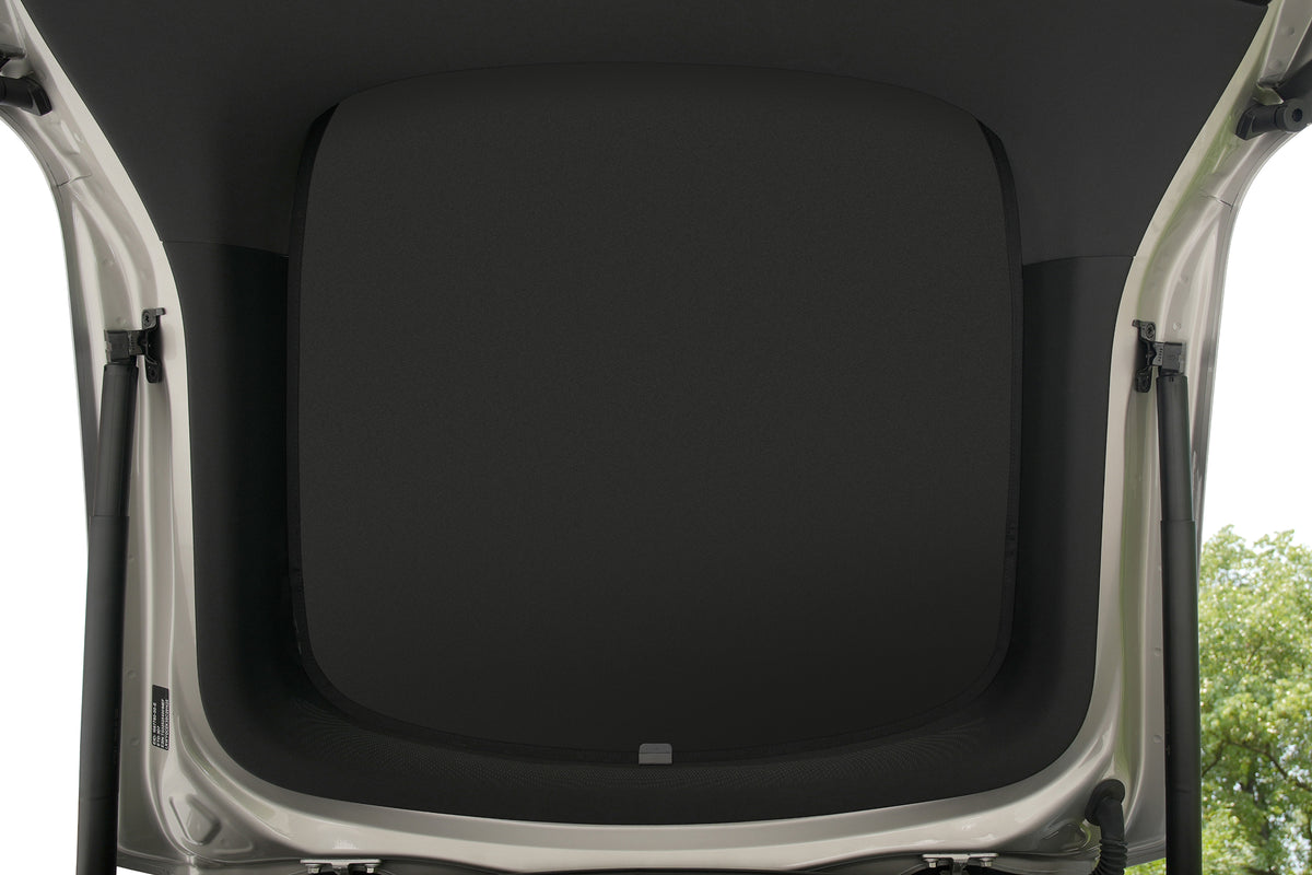View from inside an open car trunk, showing the interior lining with the trunk lid raised. The JOWUA Side + Rear Lift Gate Window Sunshade for Model Y L (2026+) can help keep this area cool and protected. Part of a tree and sky are visible outside.