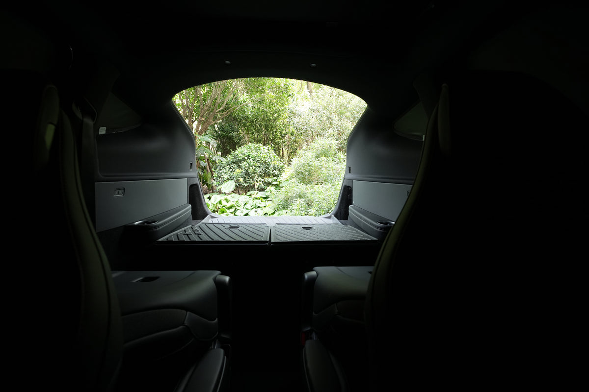 Enjoy a tranquil view from inside your Model Y L (2026+) cargo area with the back seats folded down, gazing out toward lush green trees and plants through the open hatch. The JOWUA Side + Rear Lift Gate Window Sunshade offers custom-fit comfort and privacy, making this space ideal for relaxing or securely storing your belongings.