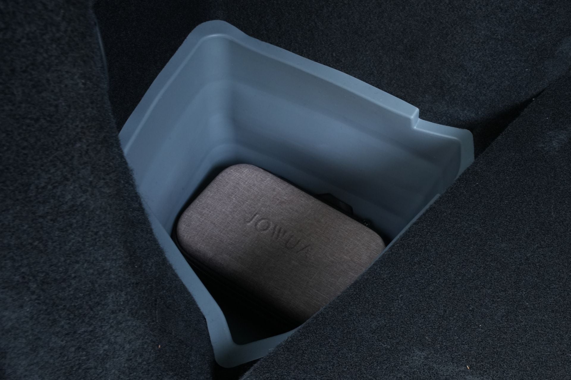 A JOWUA Tesla Model Y L (2026+) Trunk Storage Bin from the Ambient Light Bundle is positioned in the storage compartment of a Model Y L trunk, holding a fabric-covered case featuring the 
