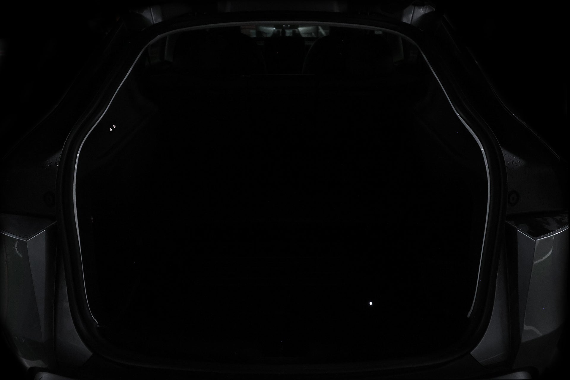 A car trunk is open, but the interior is almost completely dark, with only the outline and faint JOWUA Type-C Ambient Light & 3 in 1 Car Charger for Tesla Model Y visible.