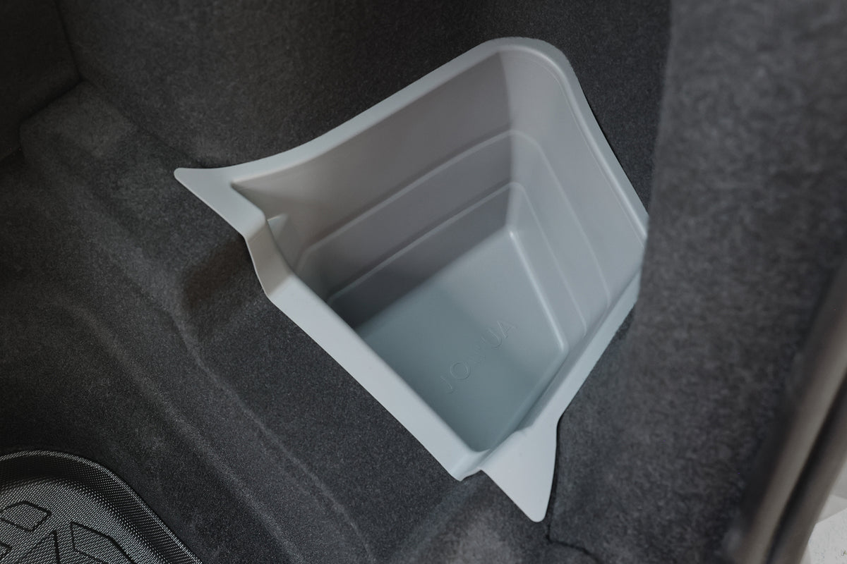 A gray plastic bin sits in a car trunk corner, surrounded by JOWUA Model Y 2025+ Interior / Trunk Full Coverage Liner Combo for added protection, with dark carpeted panels and contoured liners completing the setup.