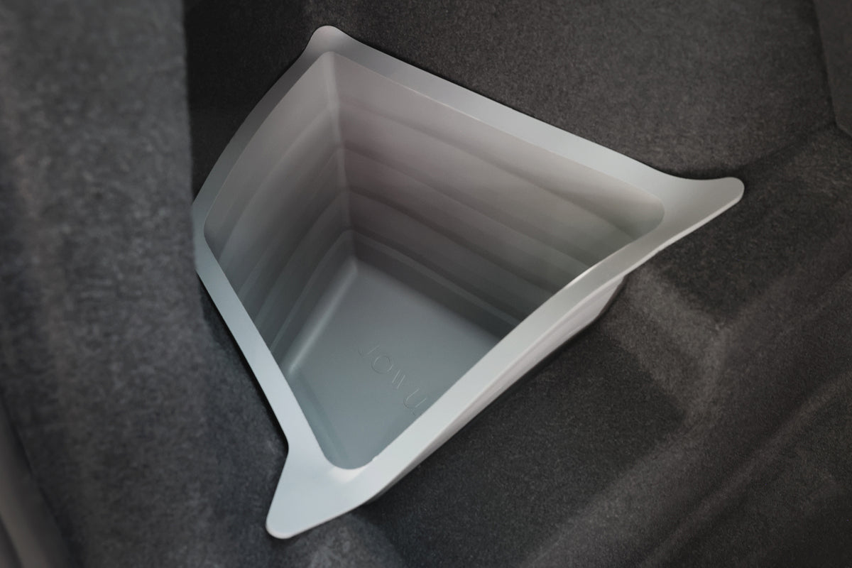 A gray, collapsible storage bin sits in the car trunk, fitting snugly atop JOWUA’s Model Y 2025+ Interior / Trunk Full Coverage Liner Combo that protects the dark carpeted interior and all-weather floor mats.