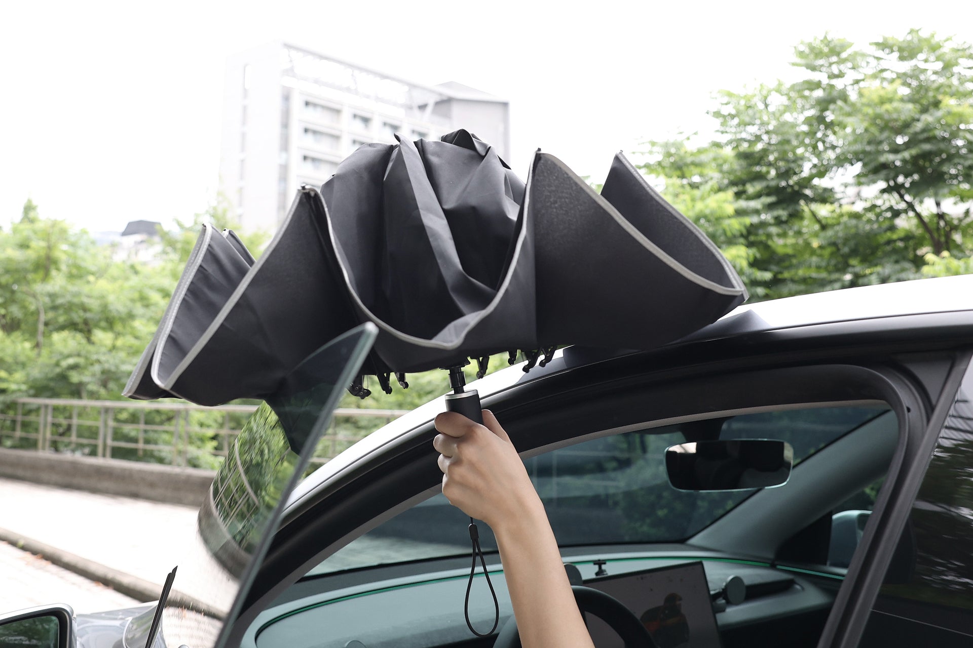 A person holds a partially open JOWUA Type-C Electric Umbrella, black in color, outside a car window with trees and buildings visible in the background.