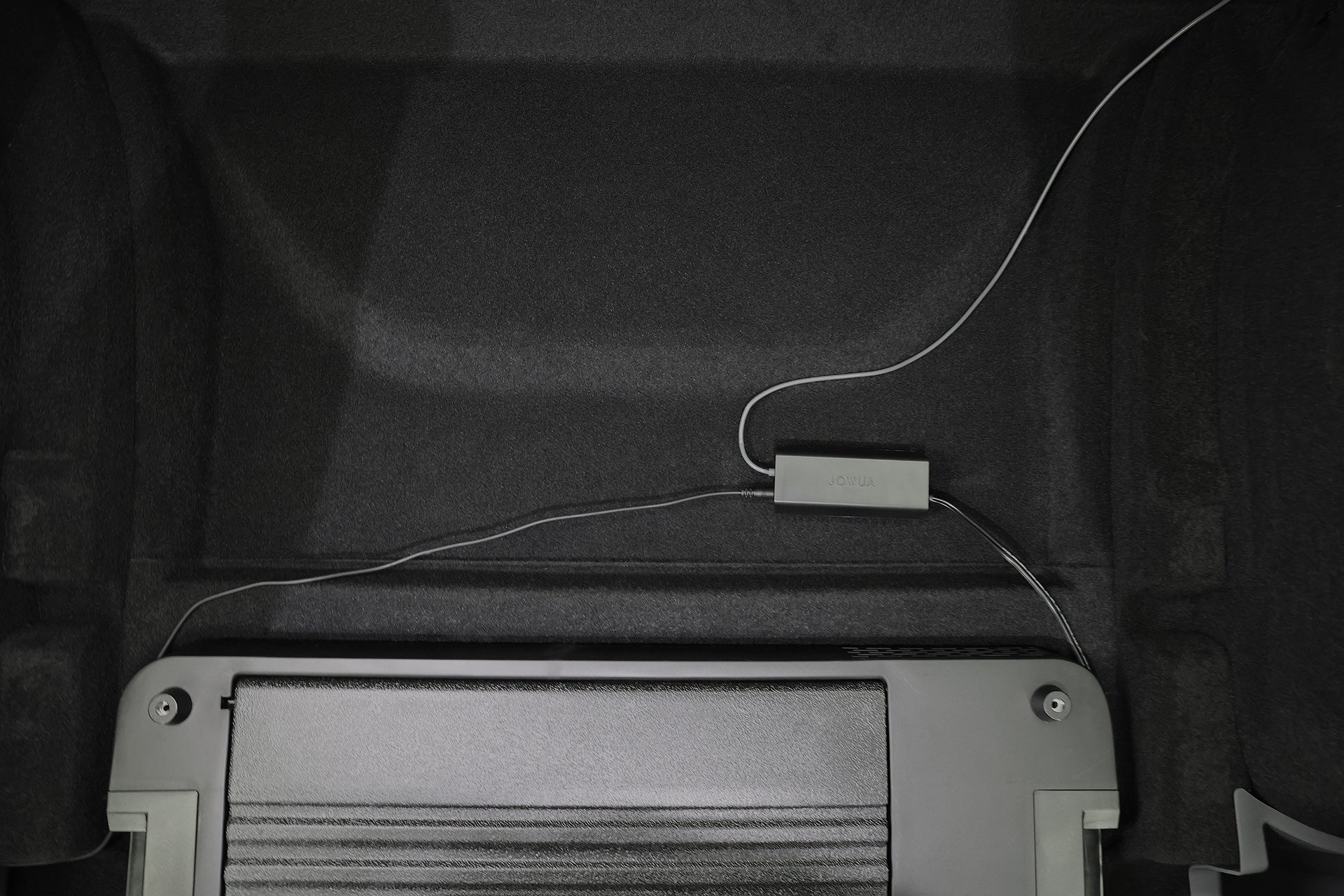 A gray JOWUA Car Refrigerator for Tesla Model Y with USB-C power mode and a connected cable sits on the black carpeted floor of a car trunk or storage compartment.