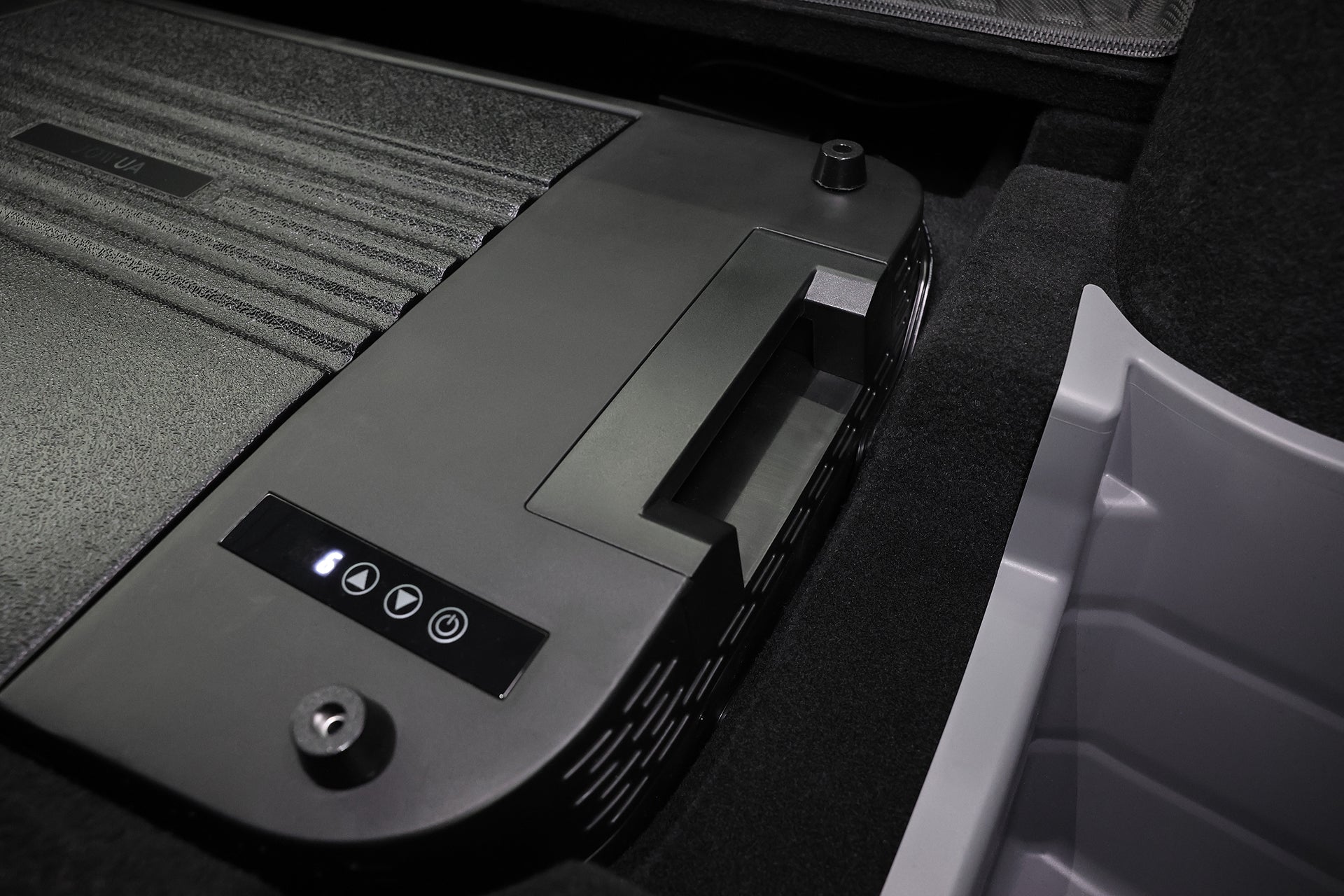 Close-up of the JOWUA Car Refrigerator for Tesla Model Y, a black device with handle, control buttons, and indicator lights, featuring intelligent dual-mode cooling, installed in a dark compartment beside a gray plastic bin.