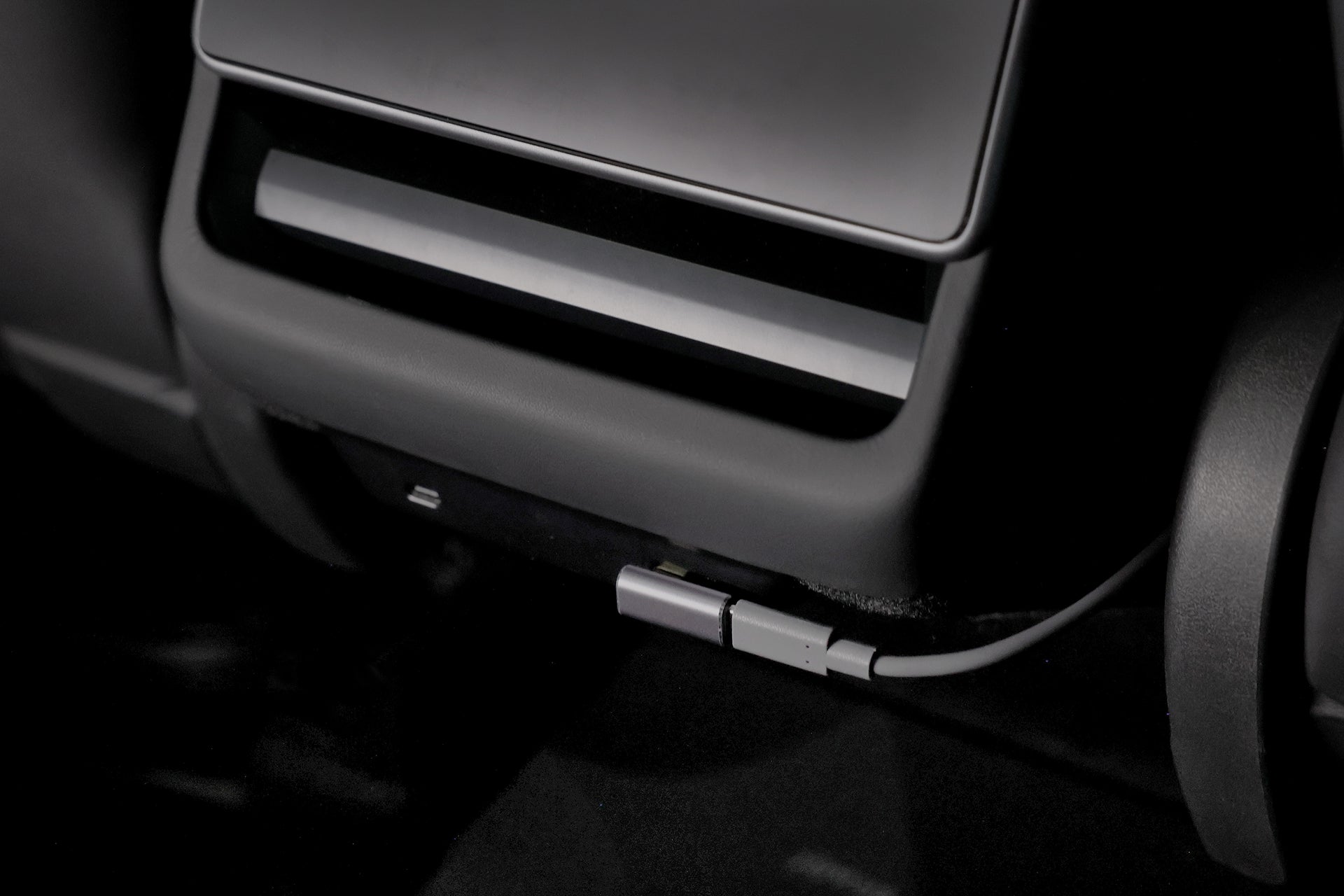 Close-up of a USB-C cable securely plugged into the JOWUA Car Refrigerator for Tesla Model Y beneath the dashboard, surrounded by a matte black finish.
