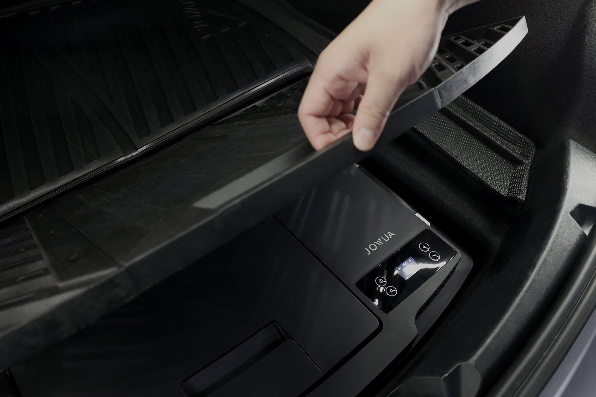 A hand lifts a trunk compartment cover, revealing a JOWUA Car Refrigerator for Tesla Model 3 (Premium/Performance 2024-2026+), a black device with display screen and buttons, featuring an intelligent dual-mode cooling system, neatly stored underneath.