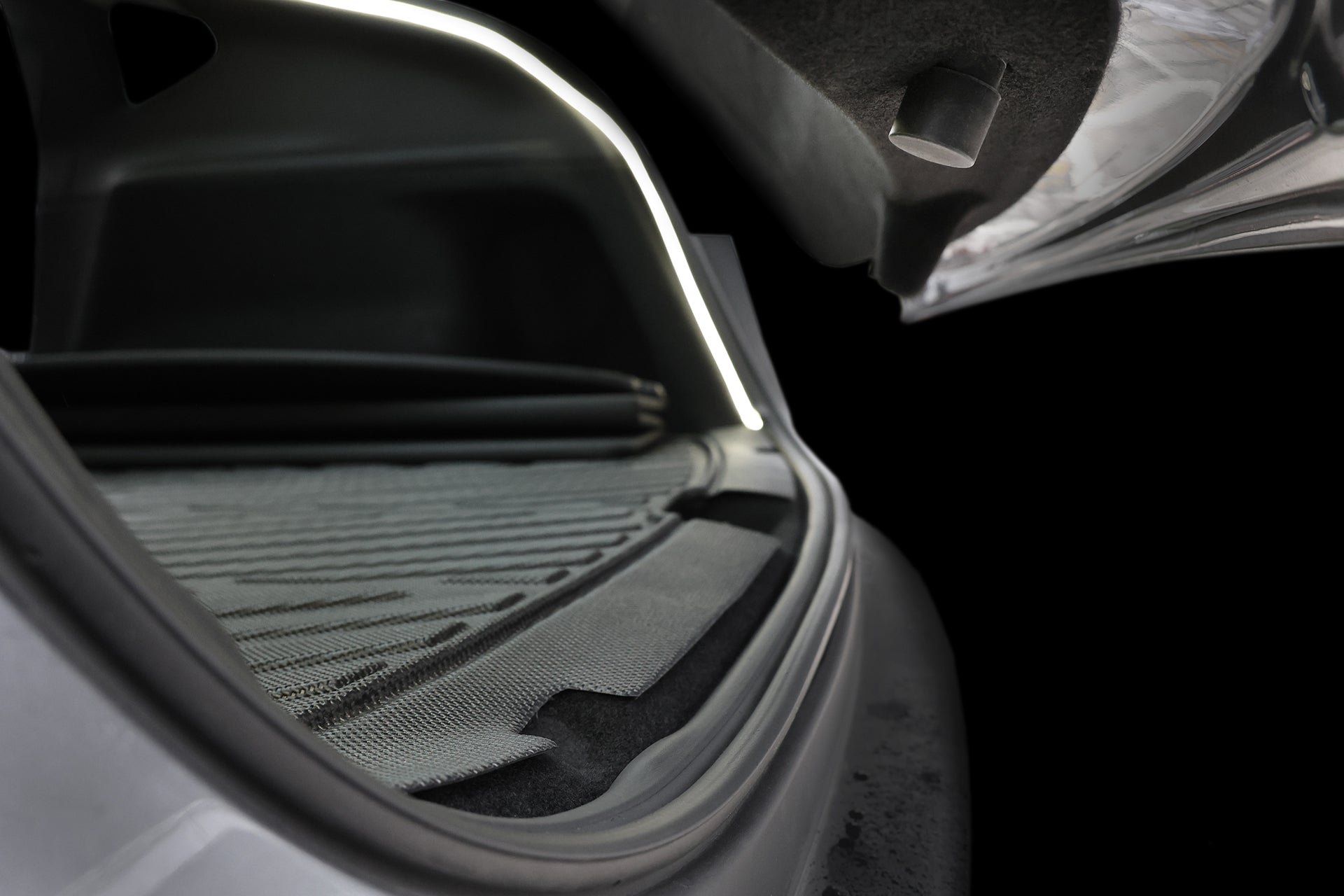 Close-up of a Tesla Model Y trunk with the lid open, showing a JOWUA USB-C LED Strip ambient light, textured rubber cargo mat, and dark interior. The bright LED highlights the spacious area against a black background.