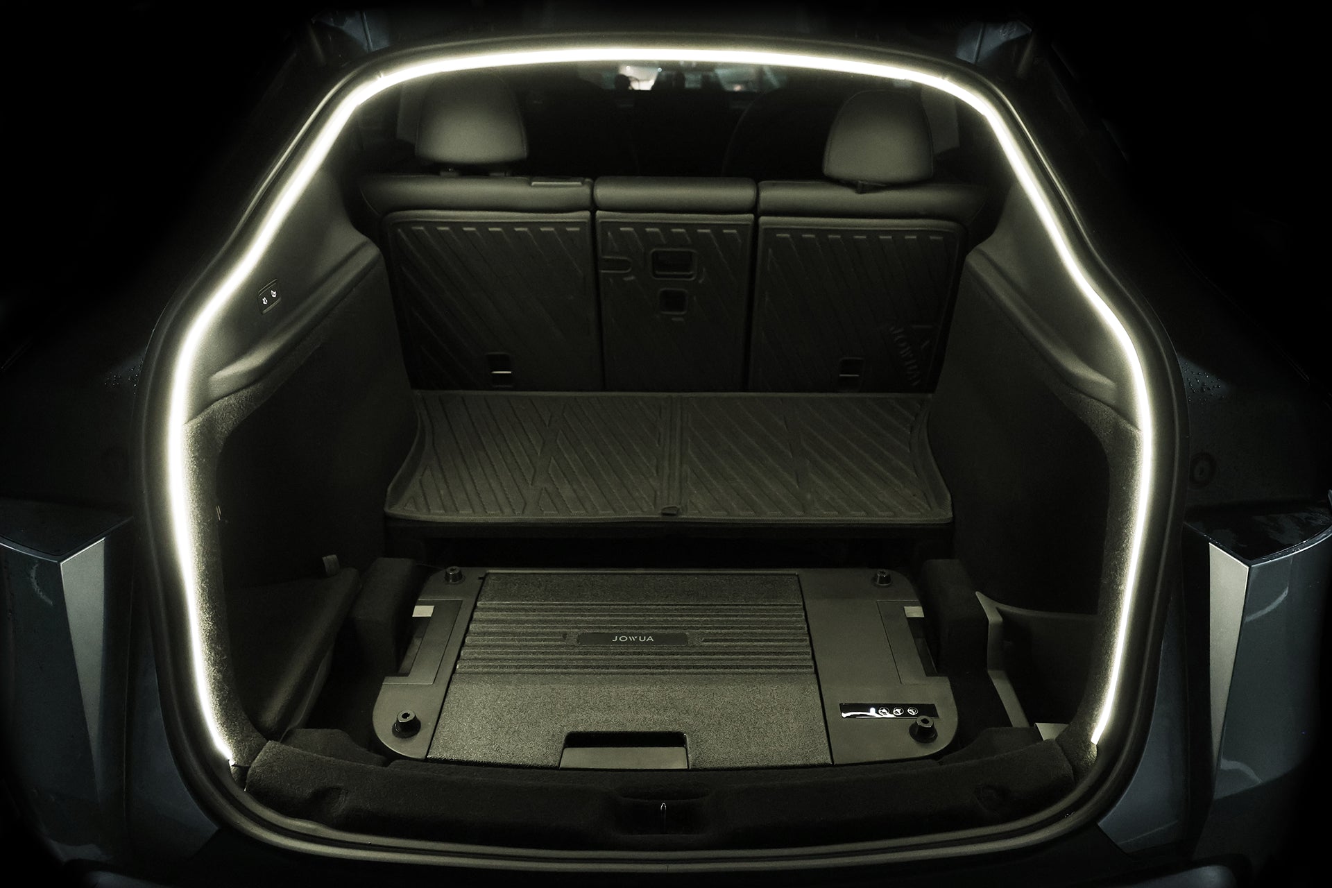 The image shows the cargo area of a Tesla Model Y with its rear hatch open, featuring the JOWUA Type-C Ambient Light & 3 in 1 Car Charger and a flat, carpeted floor with an underfloor storage compartment.