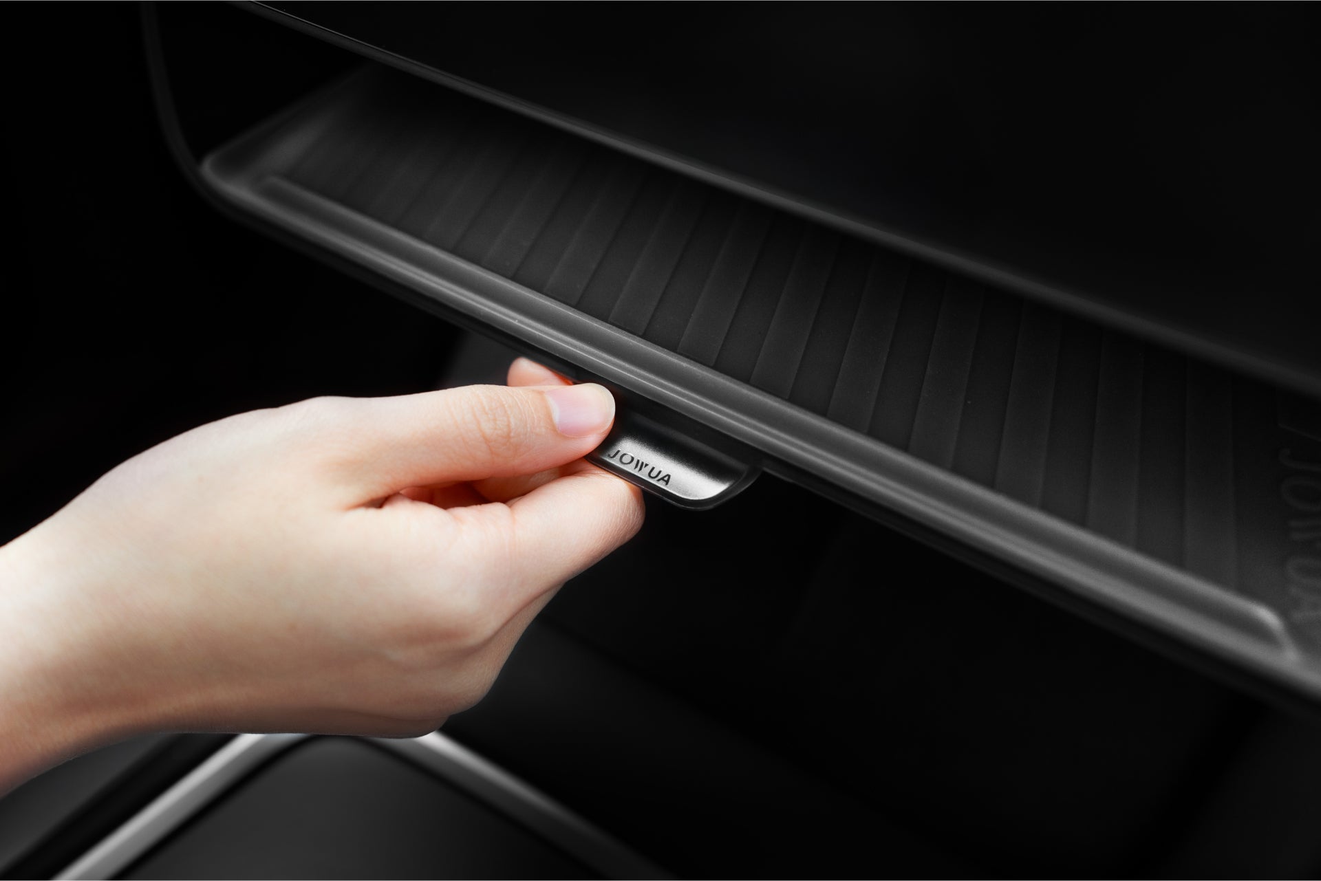 A hand reaches to open JOWUA’s Under Screen Invisible Station for Model 3 Highland (2024+)/Y Juniper (2025+), highlighting its sleek, minimalist design without visible latches.