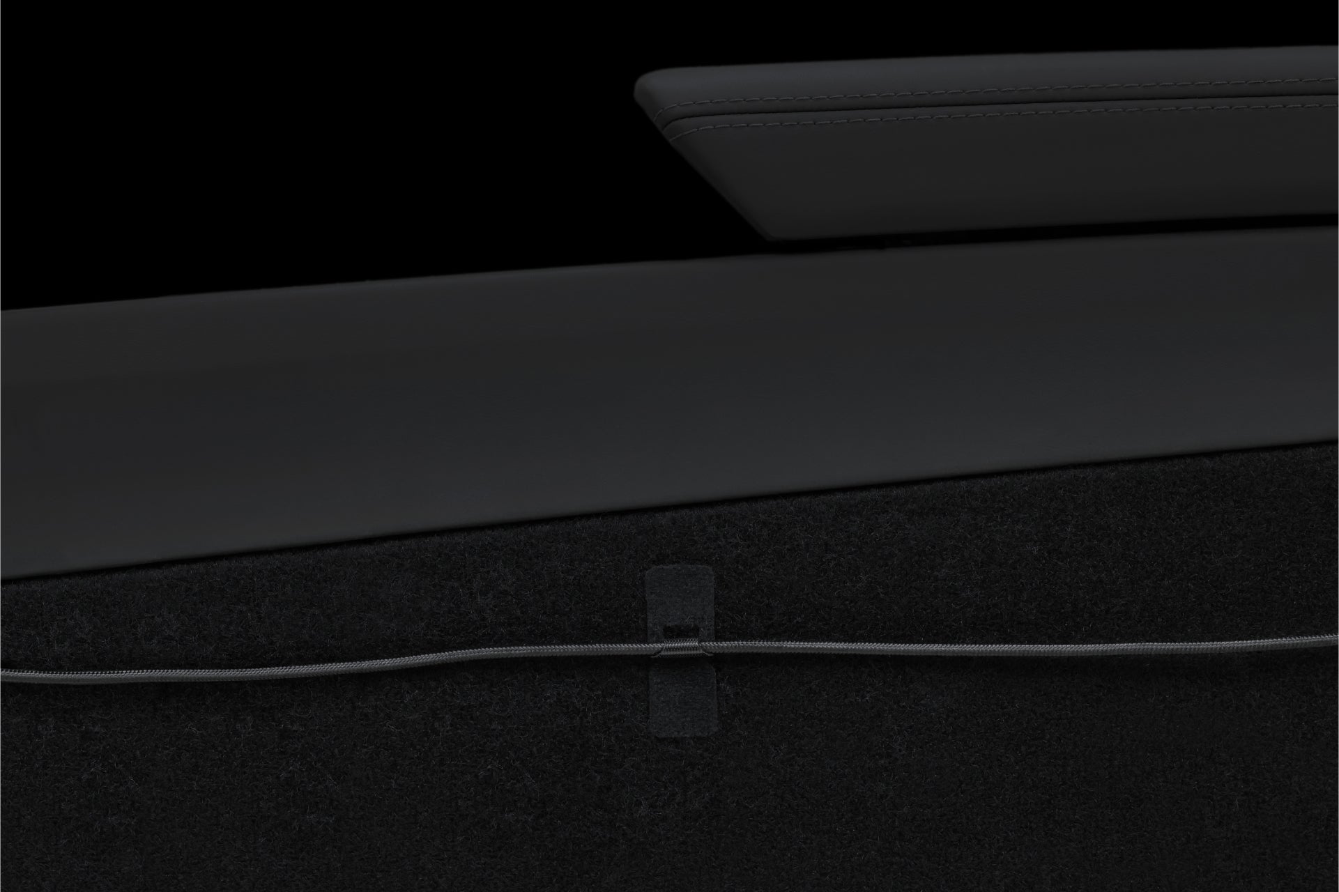 Close-up of a black interior car panel with a sleek armrest above a dark carpeted surface. A JOWUA Magnetic Charging Cable USB-C to USB-C (1M-1.8M) runs horizontally across the carpet, secured in place by a small strap—a subtle nod to Tesla Model 3 accessories.