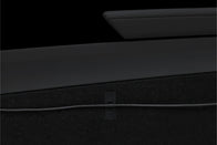 Close-up of a black interior car panel with a sleek armrest above a dark carpeted surface. A JOWUA Magnetic Charging Cable USB-C to USB-C (1M-1.8M) runs horizontally across the carpet, secured in place by a small strap—a subtle nod to Tesla Model 3 accessories.