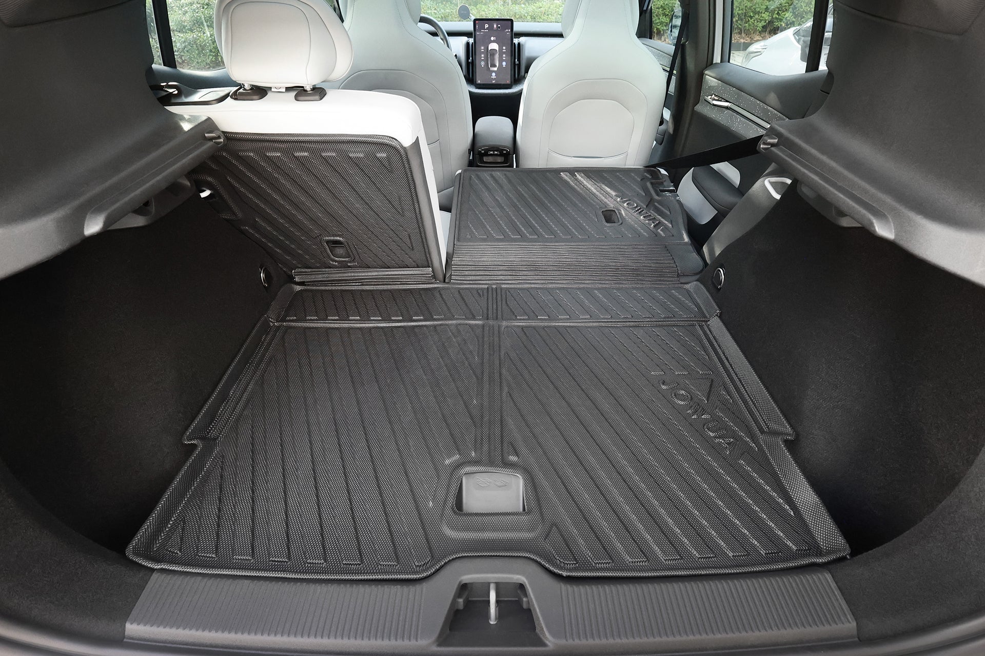 View of a Volvo EX30’s rear cargo area with back seats folded flat, featuring the JOWUA All Weather Trunk Liner + Rear Seat Cover and a touchscreen visible on the dashboard.