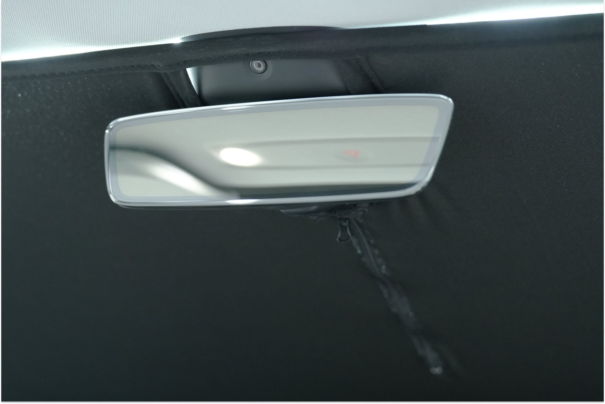 The image features an up-close view of a rectangular rearview mirror within a Tesla Model 3, encircled by dark headliner fabric. The reflection highlights the car
