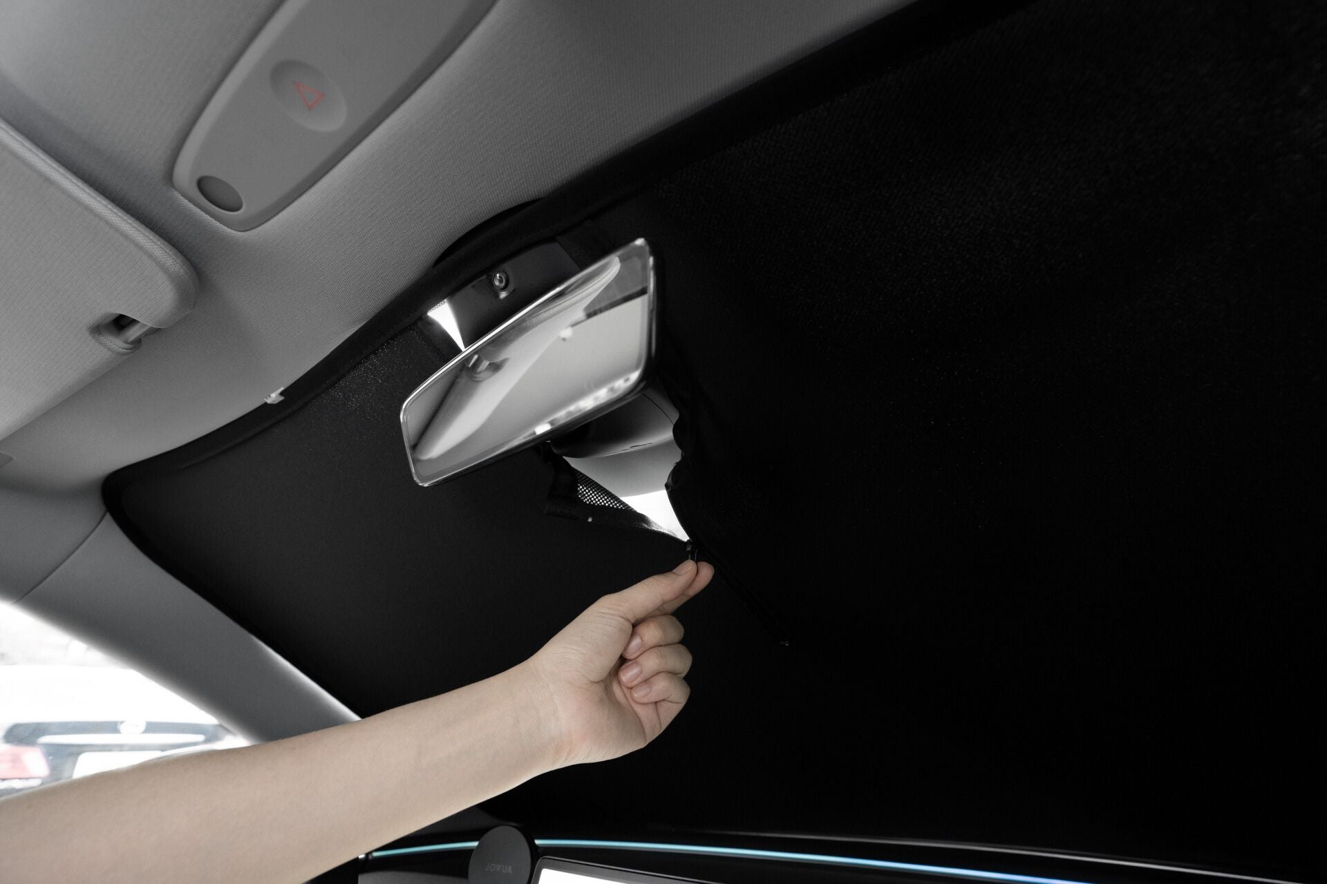 A person is seen adjusting the roof lining of a Tesla Model 3 interior with their hand visible near a small opening. The scene features the car