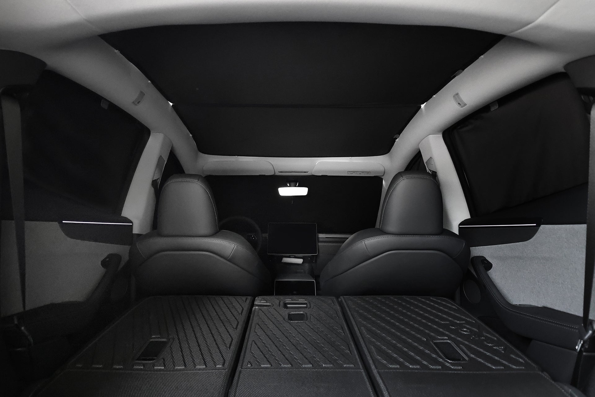 With rear seats folded flat, the car’s spacious cargo area features black leather seats, a central touchscreen, and JOWUA Side + Rear Liftgate Window Sunshade for Model Y Juniper (2025+), enhancing privacy and creating a dark interior.