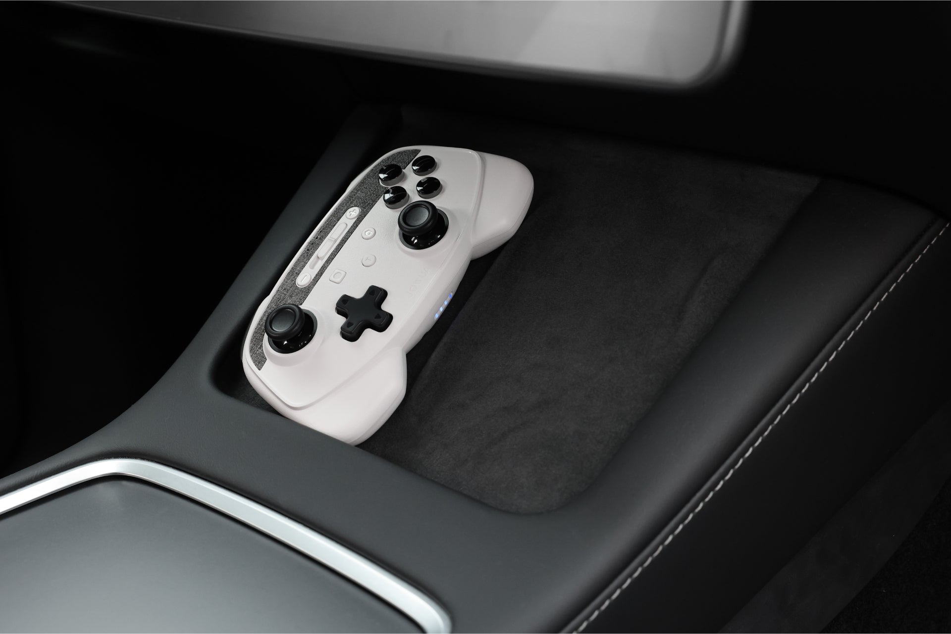 A JOWUA Wireless Tesla Game Controllers Combo for Model 3 (2018-2023) and Model Y (2018-2024) sits on a dark surface beside a silver console, highlighting sleek in-car entertainment accessories.