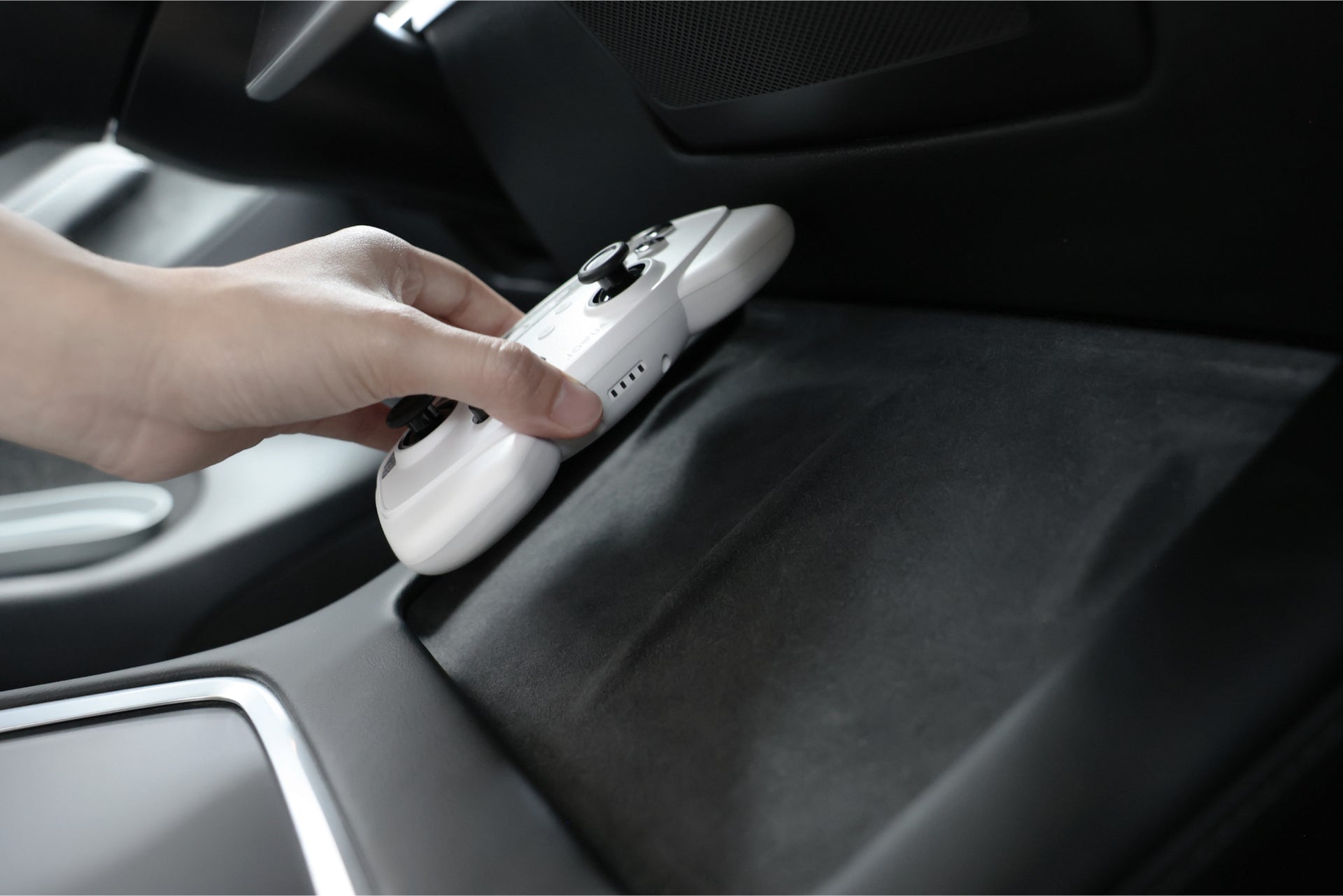 A hand sets a JOWUA Wireless Tesla Game Controllers Combo on a black surface inside a Tesla Model 3, near the center console—perfect for wireless charging and use with compatible 2018-2023 Model 3 or 2018-2024 Model Y accessories.