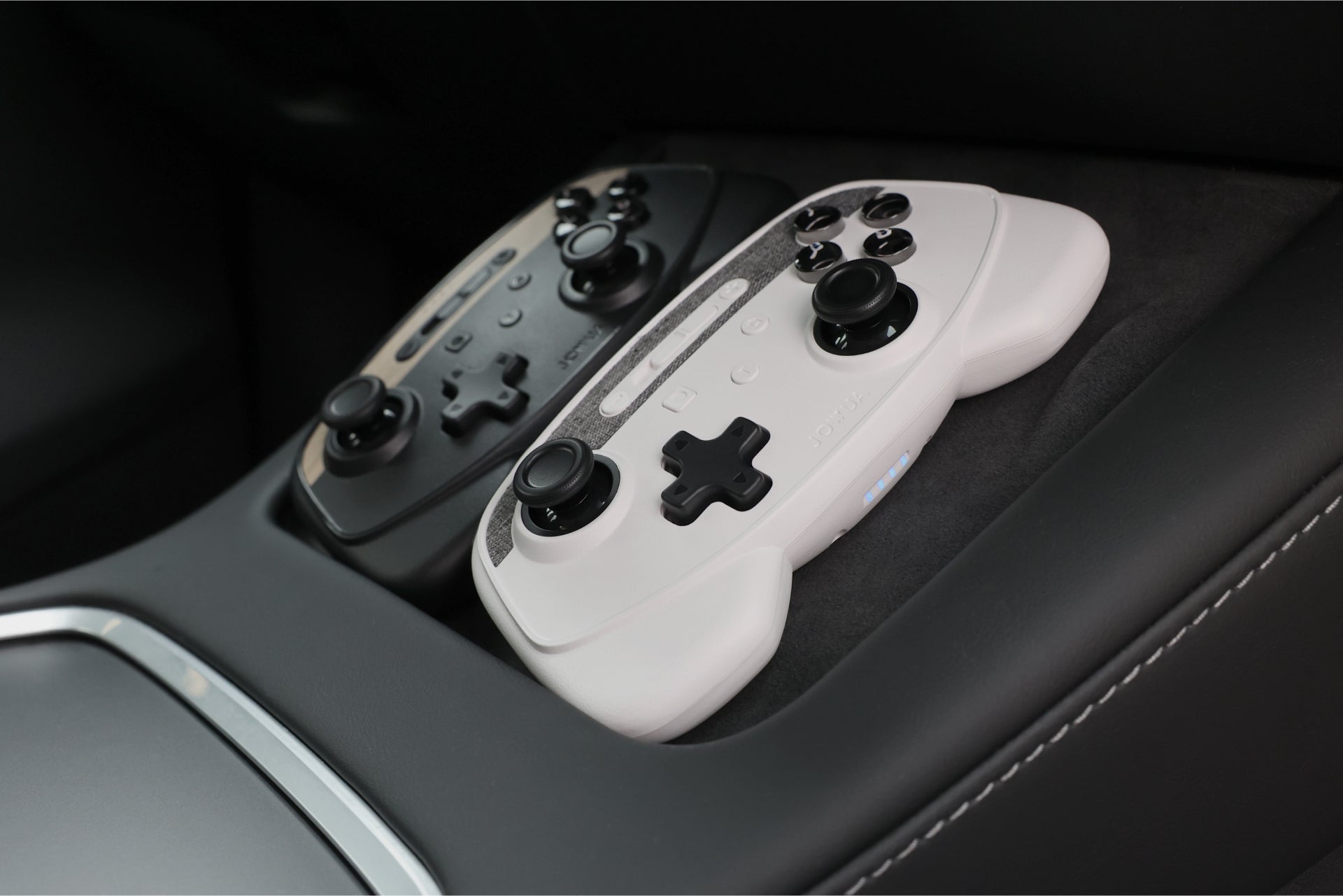 Two JOWUA Wireless Tesla Game Controllers, one black and one white, sit side by side in a Tesla Model 3's console—designed for Model 3 (2018-2023) & Model Y (2018-2024)—the perfect addition to your Tesla accessories.