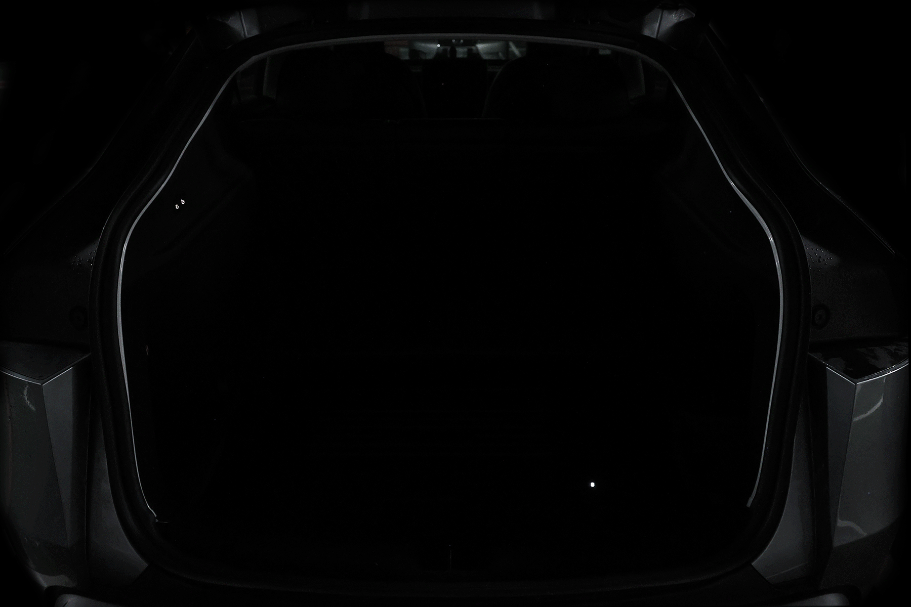 A car trunk in low light shows only faint outlines, highlighting the need for the JOWUA Type-C Ambient Light & 3 in 1 Car Charger designed for Tesla Model Y.