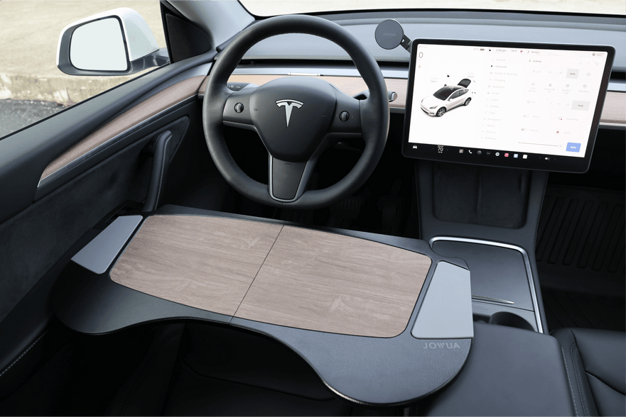 The car interior showcases a Tesla logo on the steering wheel and includes a large touchscreen displaying essential information. It features a wooden lap desk on the driver's seat and is highlighted by premium materials. This setup is further enhanced with JOWUA's Foldable Car Tray for Tesla, offering added versatility.