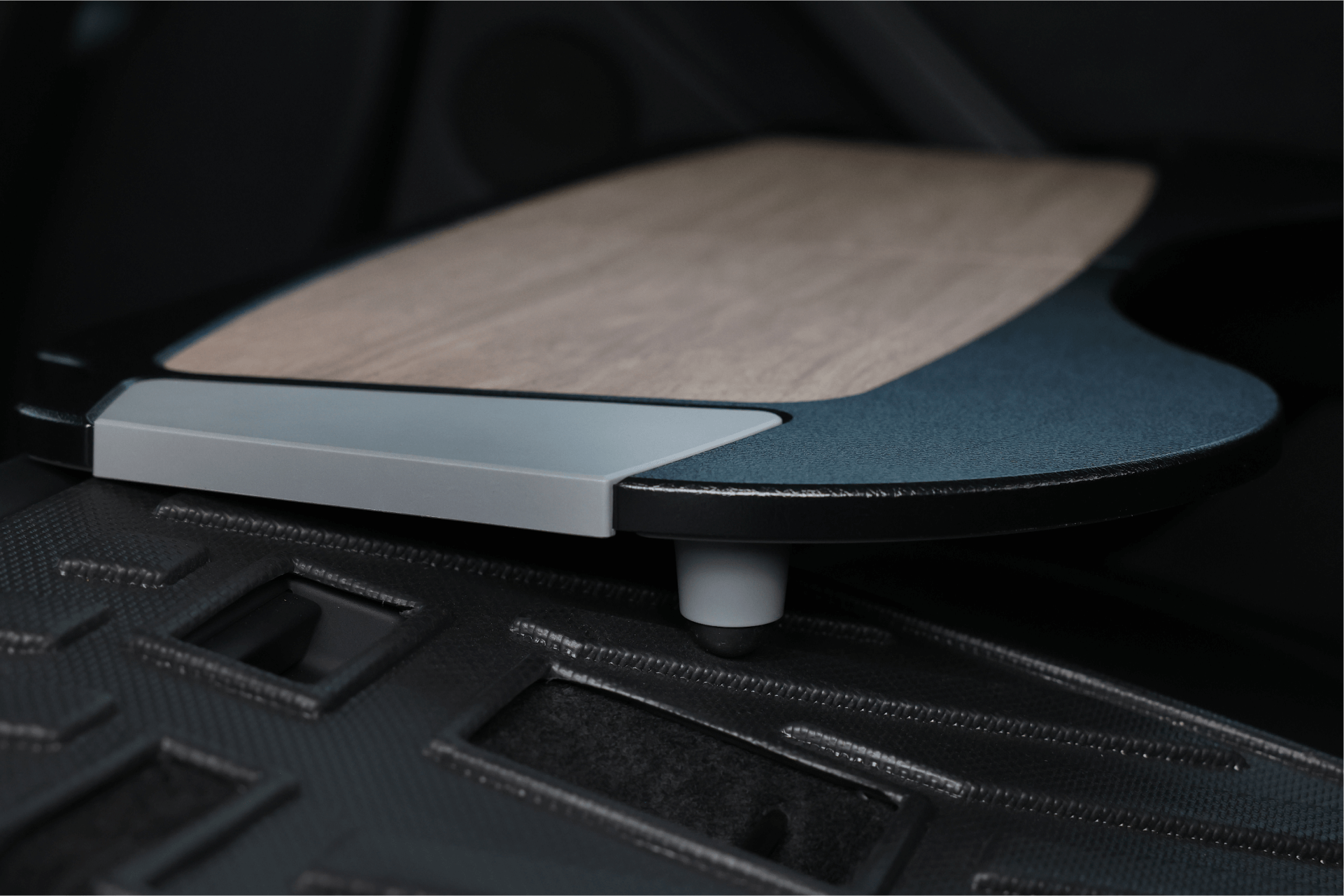 A close-up of a Tesla Model S interior showcases the JOWUA Foldable Car Tray Bundle, featuring a wooden tray with a dark frame partially extended over a textured black surface with square cutouts.