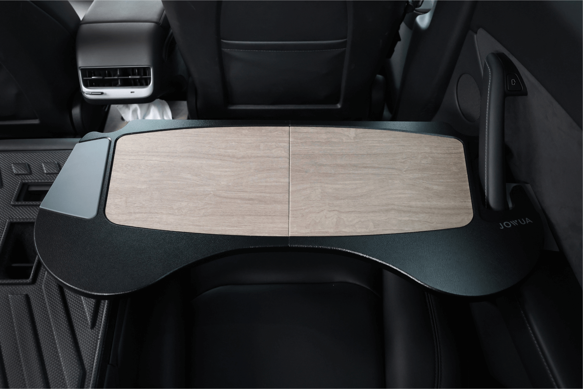 The image showcases the rear seat of a Tesla Model S with a JOWUA Foldable Car Tray Bundle. The tray's foldable design includes a sleek wooden surface that fits seamlessly between the seats, featuring the JOWUA logo elegantly placed in the corner.