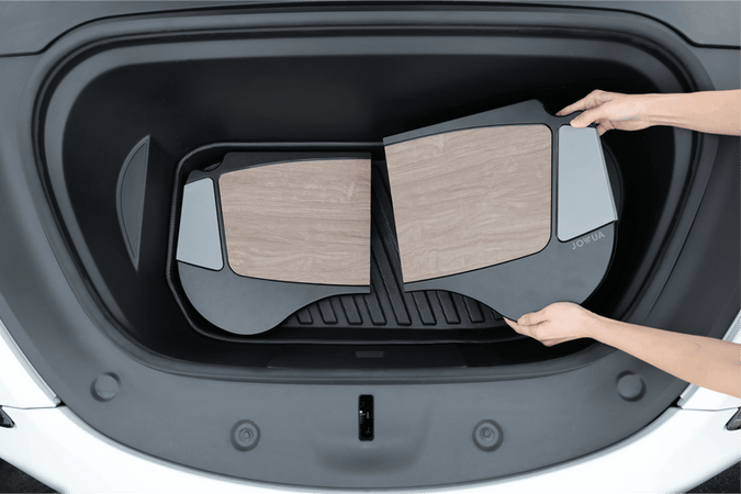 A person places two JOWUA Model 3 All Weather Trunk Combo mats, specifically designed for the reengineered Model 3 Highland (2024+), inside the trunk of their Tesla. These mats are crafted from waterproof TPE material and feature a distinctive wood-like pattern with black borders, perfectly complementing the stylish interior of their vehicle.
