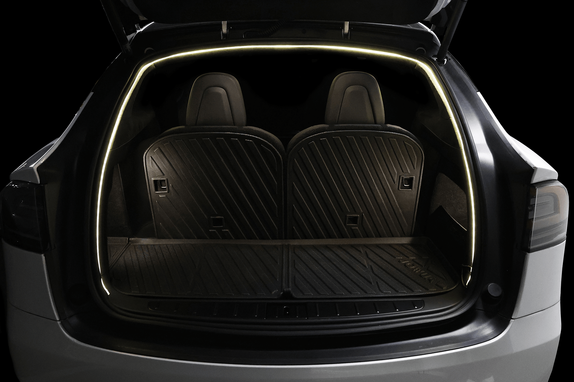 A Tesla Model X trunk features two rear seats and black custom-molded floor mats, illuminated by the JOWUA Tesla Model X Trunk Ambient Light - USB-C LED Strip along the hatch opening.