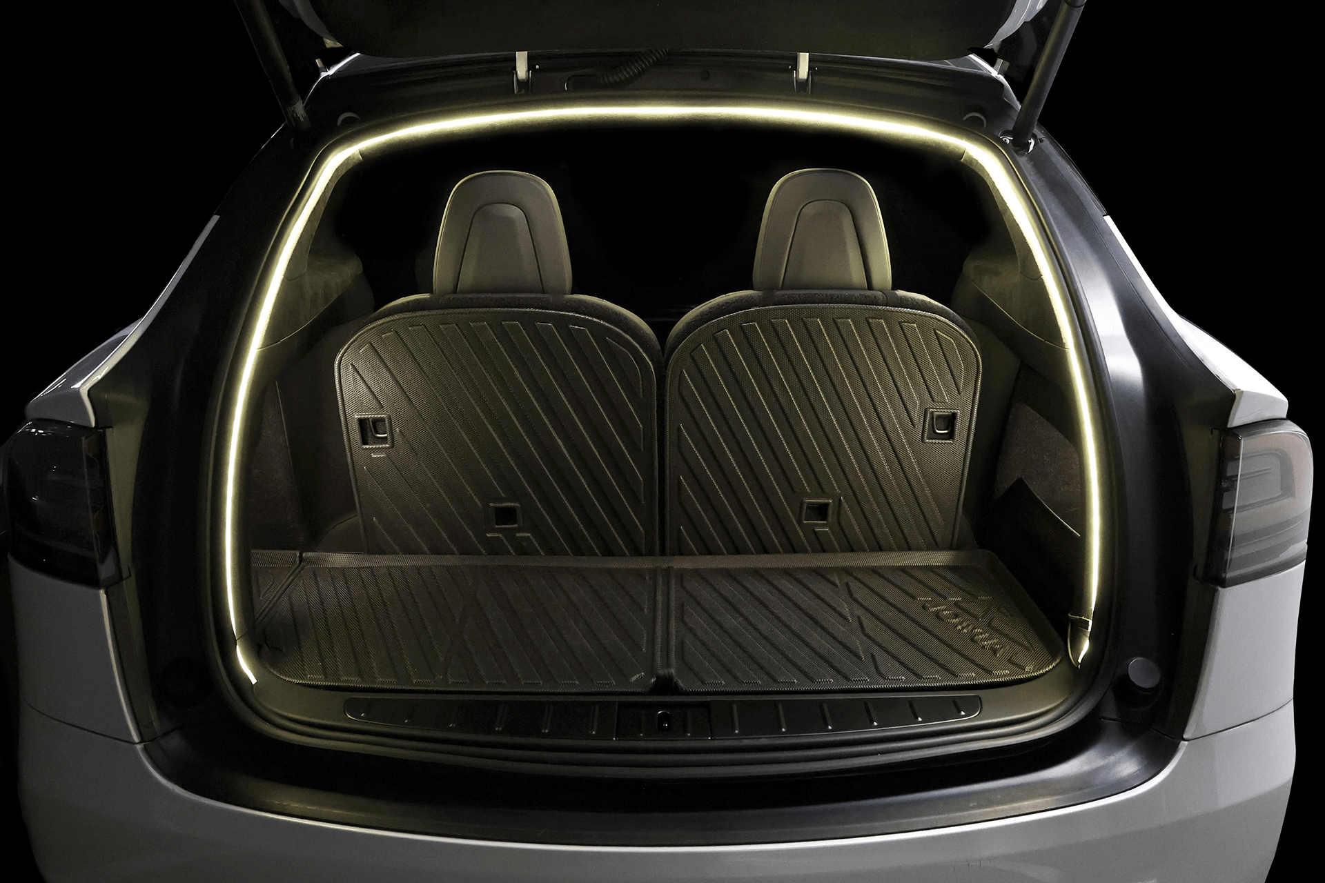 Open trunk of a Tesla Model X showing two rear seats with black rubber mats. A JOWUA Tesla Model X Trunk Ambient Light - USB-C LED Strip outlines the trunk using magnetic induction, brightly illuminating the interior.