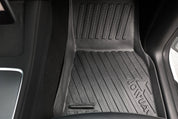 A close-up of a black rubber car floor mat with the "JOWUA" logo from the Premium Interior Essentials Set (RHD) – Model Y Juniper, placed on the car floor by the center console.