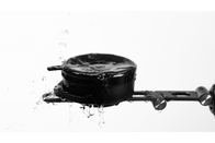 A black JOWUA 6D Tesla Compatible Invisible Foldaway Car Mount Qi2 Wireless Charger (MagSafe) is splashed with water, creating droplets on its surface. It attaches to a metallic arm on the right, set against a white background.