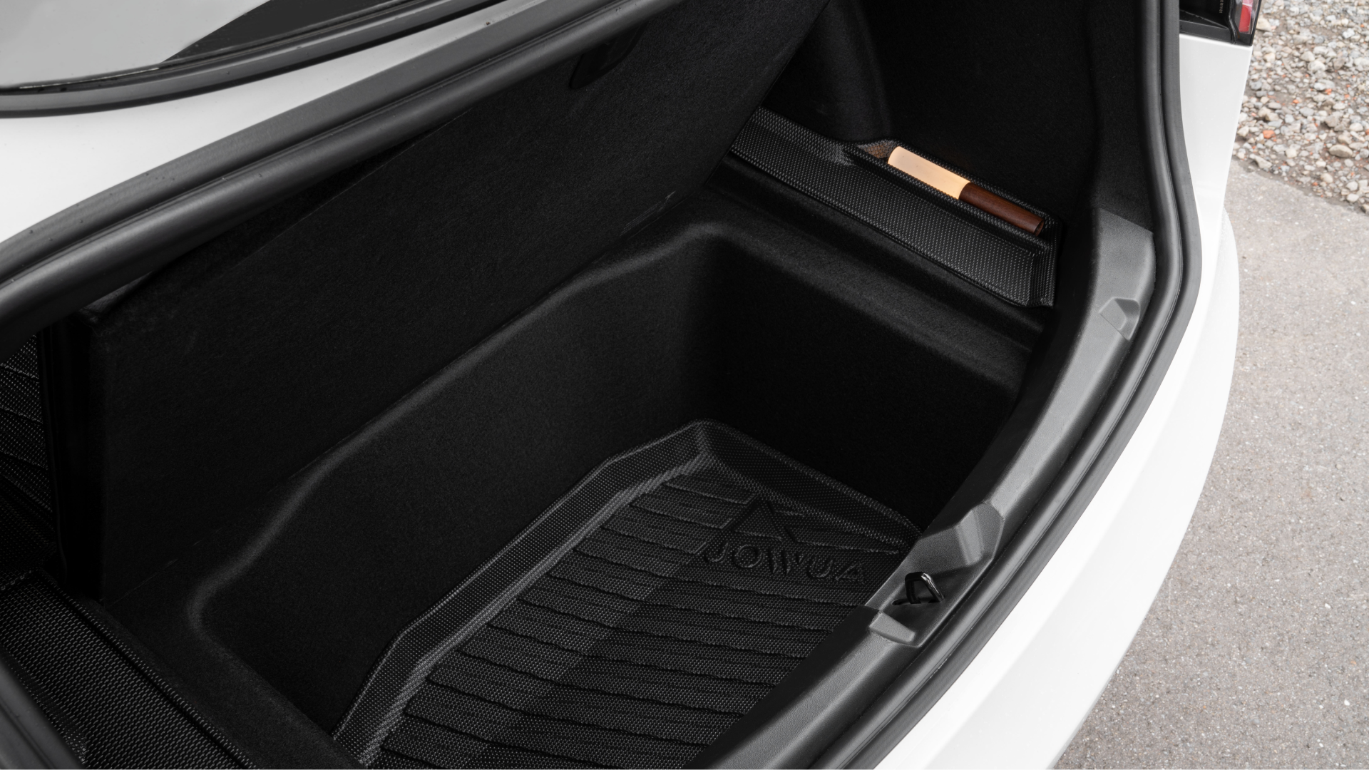 The open trunk compartment of a white Tesla Model 3 displays a spacious area equipped with a JOWUA Reengineered Model 3 All Weather Trunk Liner, set against the backdrop of gray pavement.