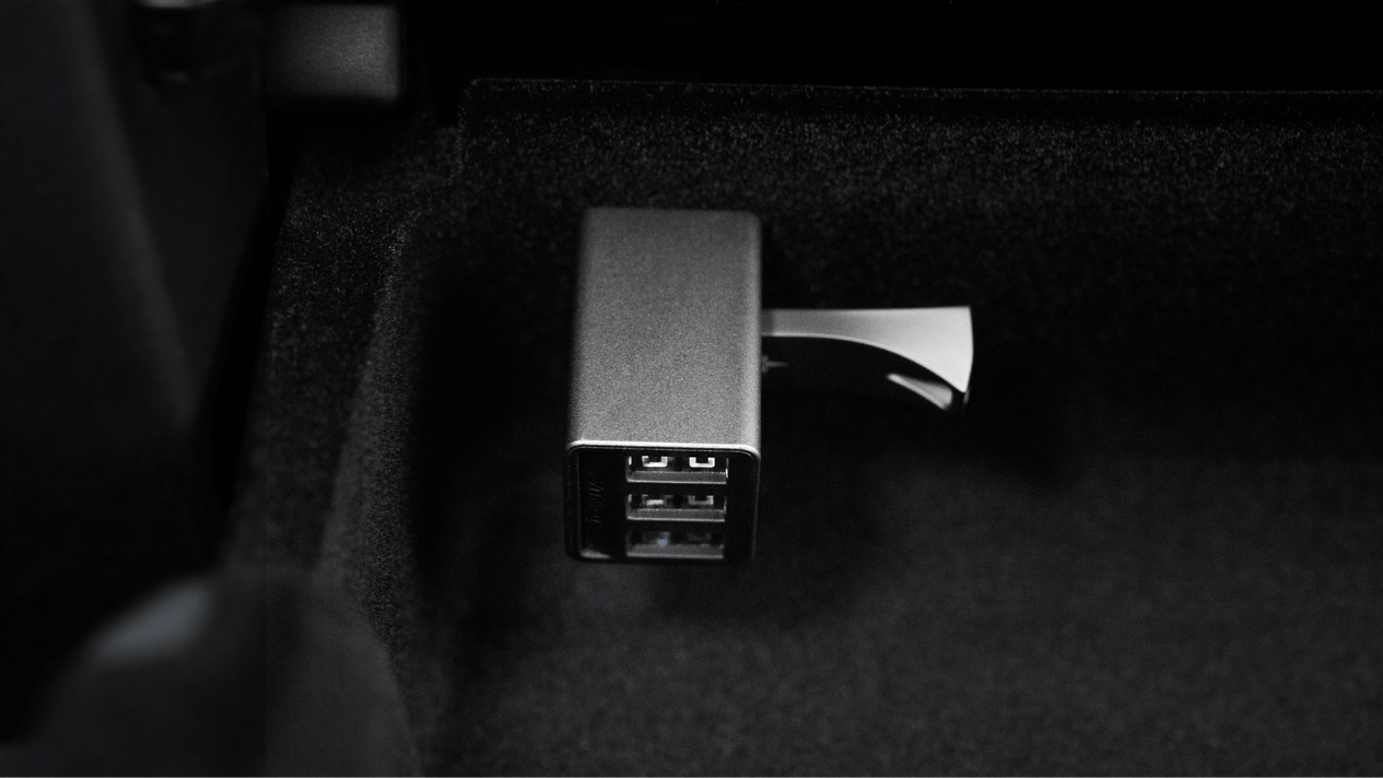 A close-up of the JOWUA 36W Hub Charging Combo on a dark surface, resembling a sleek Tesla USB Hub, with a USB drive inserted. The metallic rectangular charger displays multiple slots.