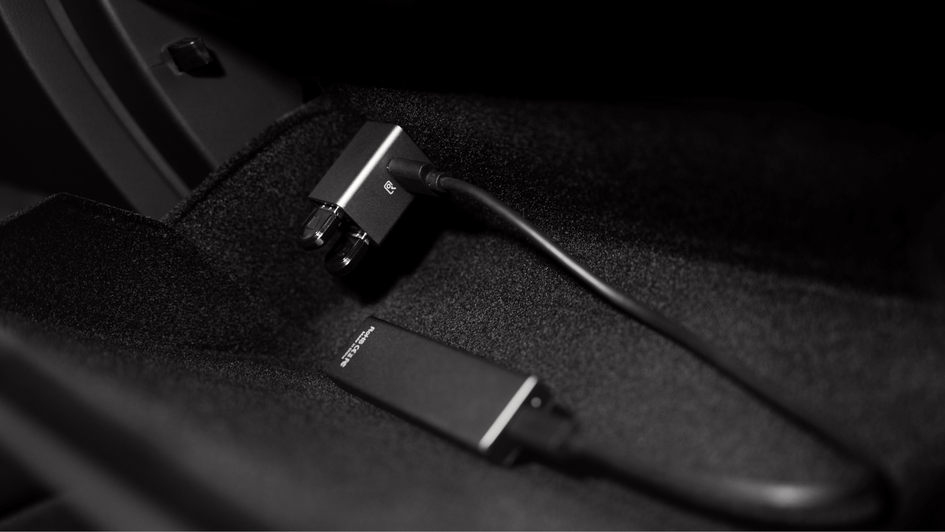 In a car's dim interior, a close-up shows the JOWUA 36W Hub Charging Combo with an attached cable resting on a dark, textured surface, highlighting the hub and cable in stark contrast.