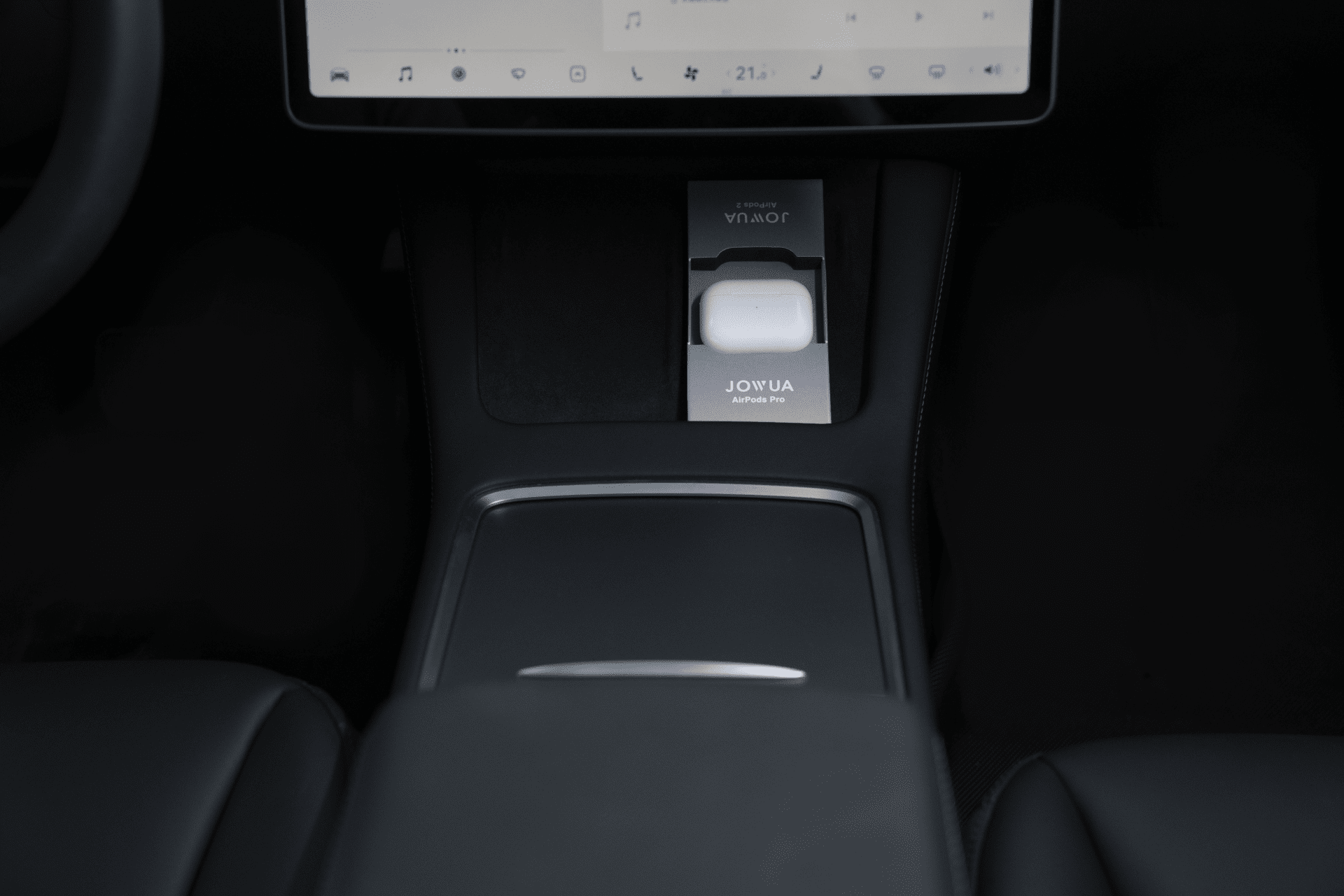 Close-up of a Tesla Model's interior highlighting a dashboard with a touchscreen display showing various icons. Below, the JOWUA AirPods Charger Stand rests on the wireless charging pad, securely holding white wireless earbuds in their case.