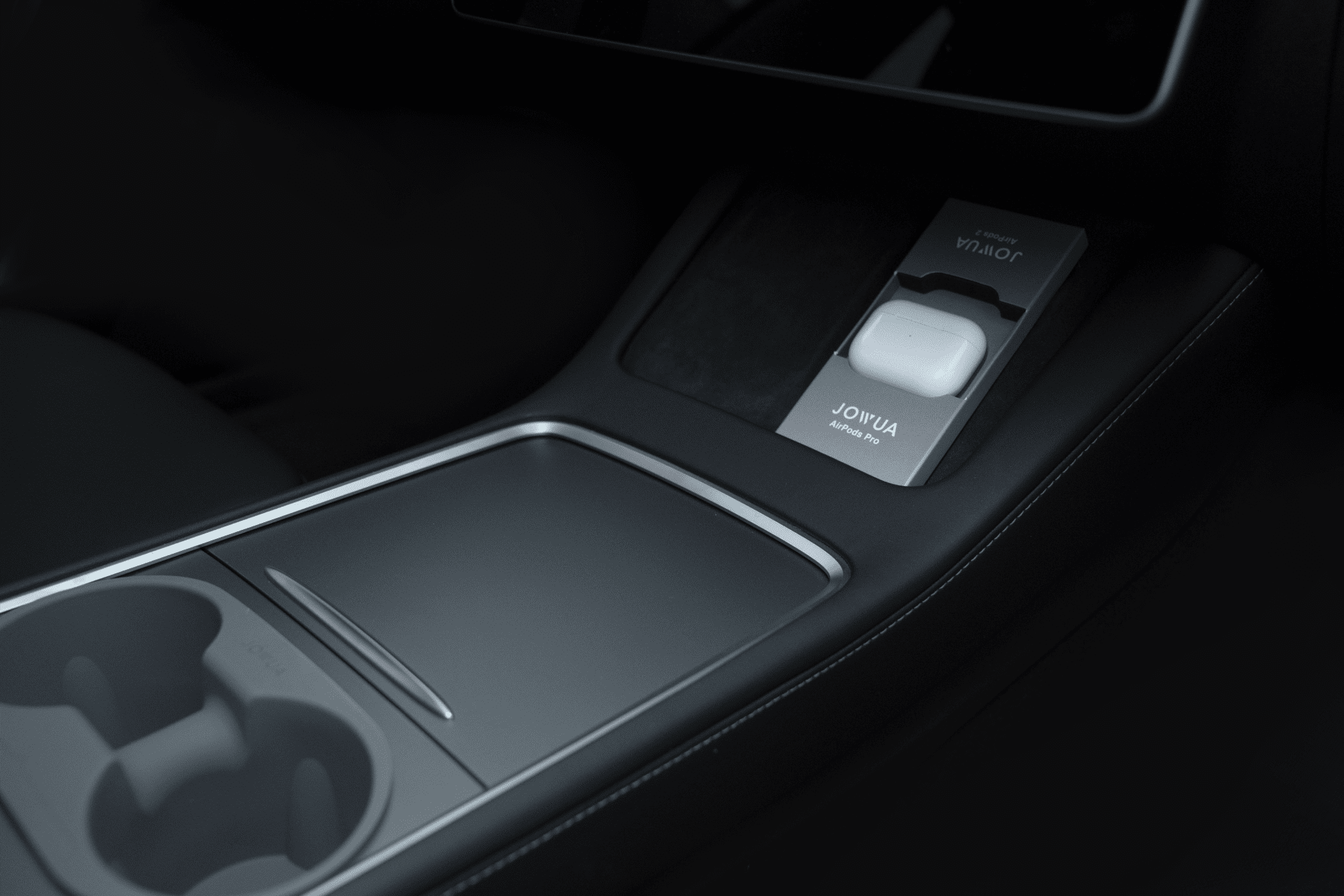 The interior of the car boasts a sleek and modern design, similar to Tesla models, featuring the JOWUA AirPods Charger Stand. This stylish piece is conveniently placed next to the cup holder and center console, alongside a wireless phone charger.