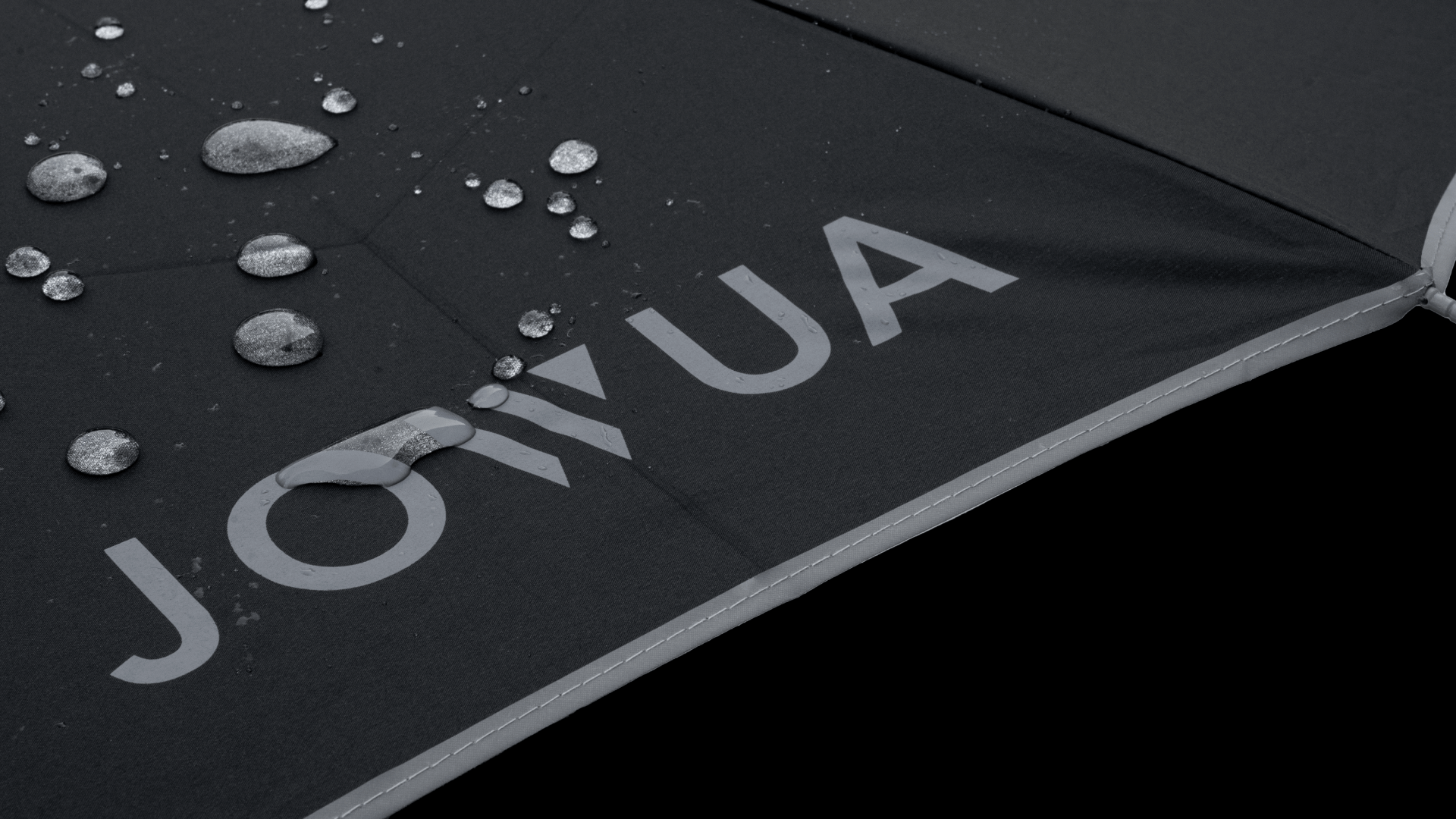 Close-up of the Tesla Color Matching Umbrella's black surface with water droplets, highlighting its water-repellency. The word "JOWUA" is printed in gray letters on the fabric, adding texture and depth to the sleek appearance of this anti-rebound inverted design.