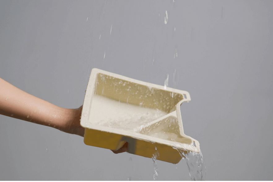 A hand holds a tilted Center Console Tray Organizer from JOWUA, designed for Tesla Model 3 / Y vehicles, crafted from premium hybrid material, with water flowing out and creating a splash against a gray background.