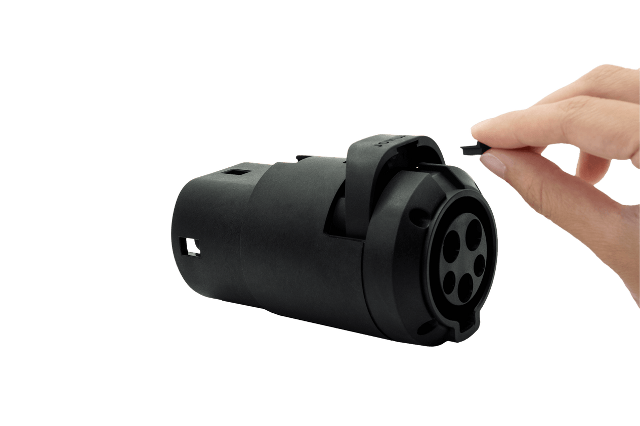 A hand is holding a black plastic cap next to a black cylindrical object featuring multiple circular ports, which appears to be the JOWUA J1772 to CCS2-AC (TYPE2) Adapter (Tesla Anti-pull), set against a plain background.