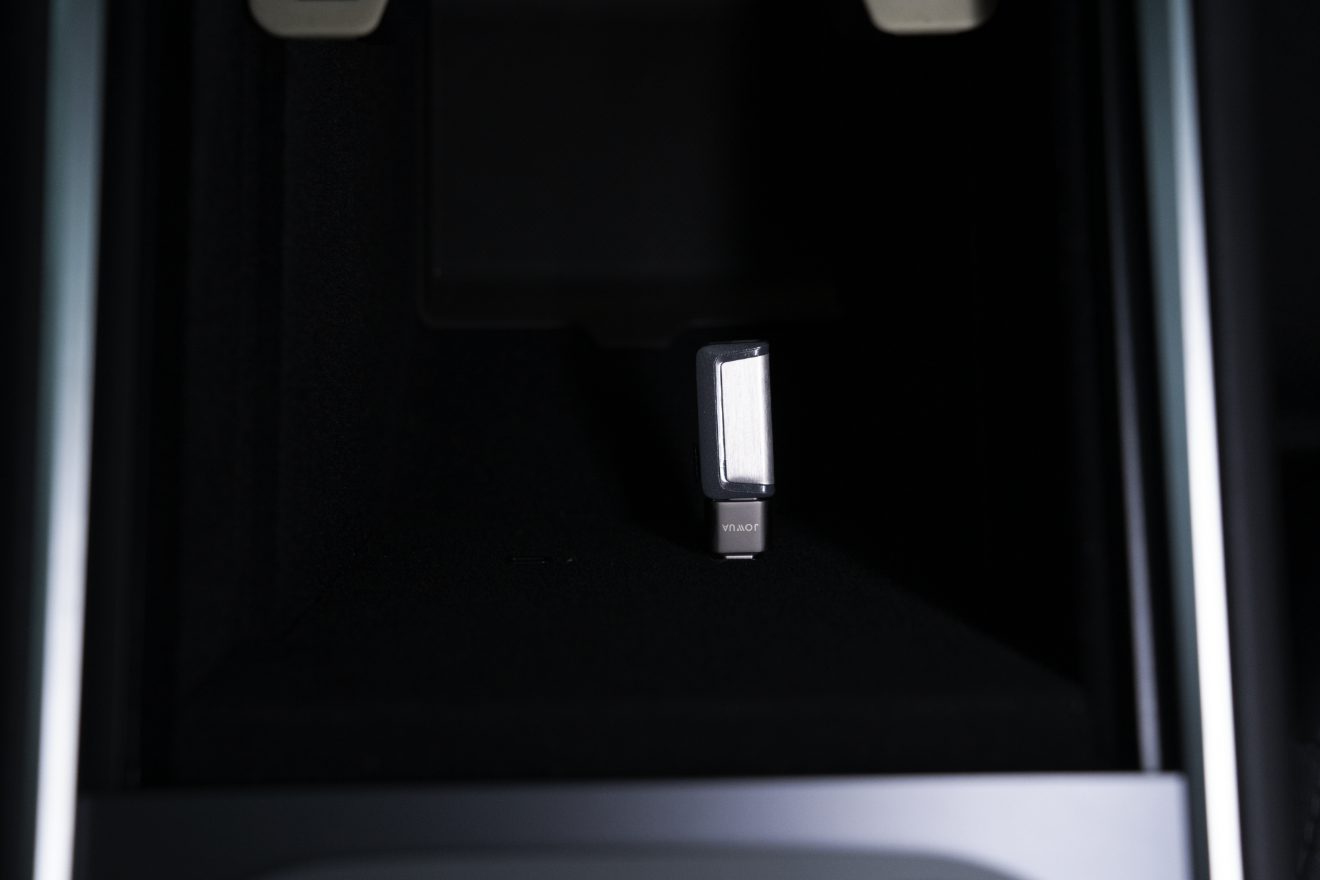 A close-up of a USB-C to USB-A Adapter(Data OTG) by JOWUA, enhanced with TeslaConnect technology, inserted into a slot within a dark compartment. The adapter has a metallic surface with "vitalBR" on its label. The compartment features metallic edges and is part of a larger electronic device.