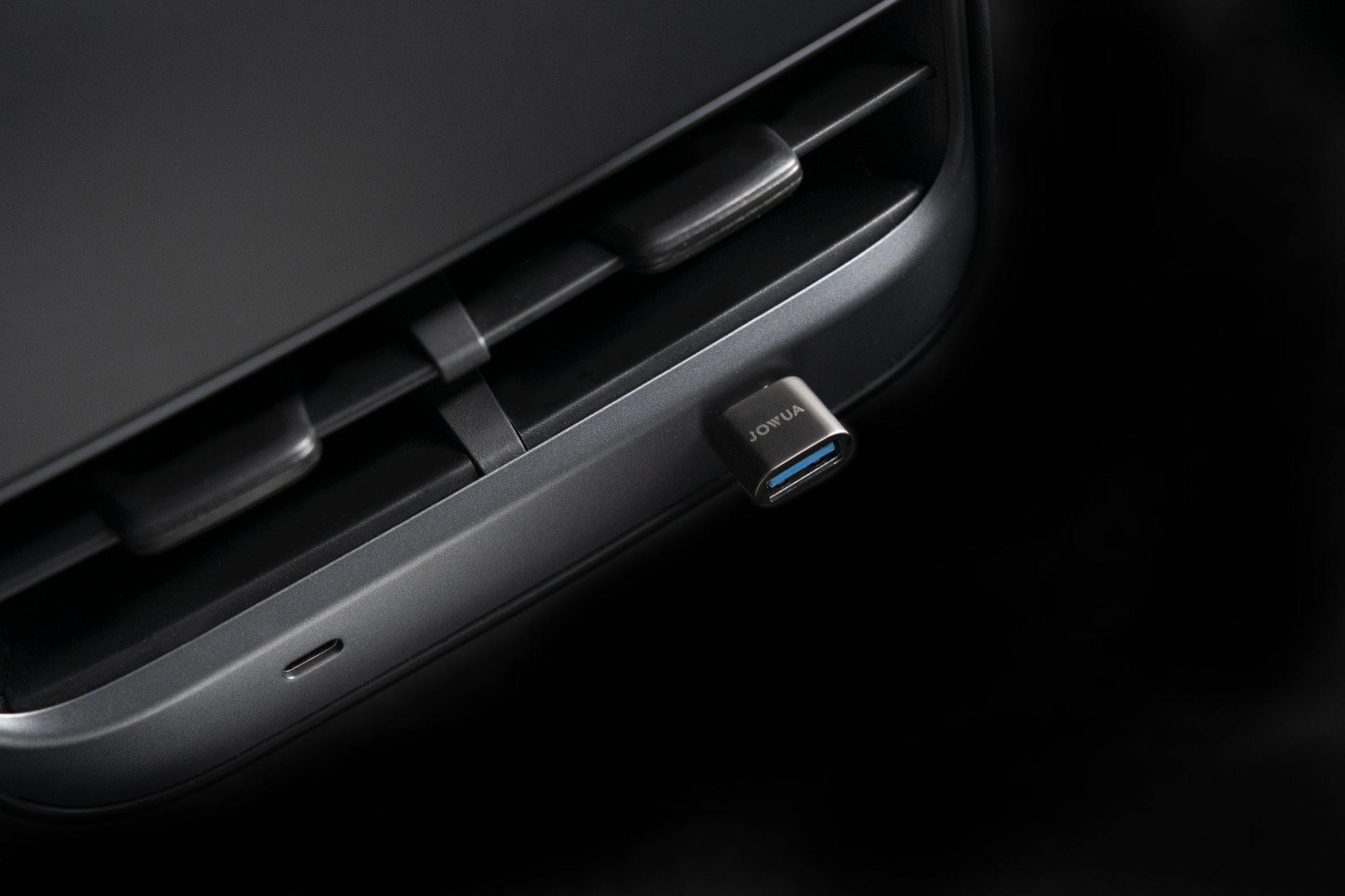 Close-up of a black USB-C to USB-A adapter plugged into a device port, set against a dark background. The adapter, perfect for data sync, proudly displays the word "JOWUA.