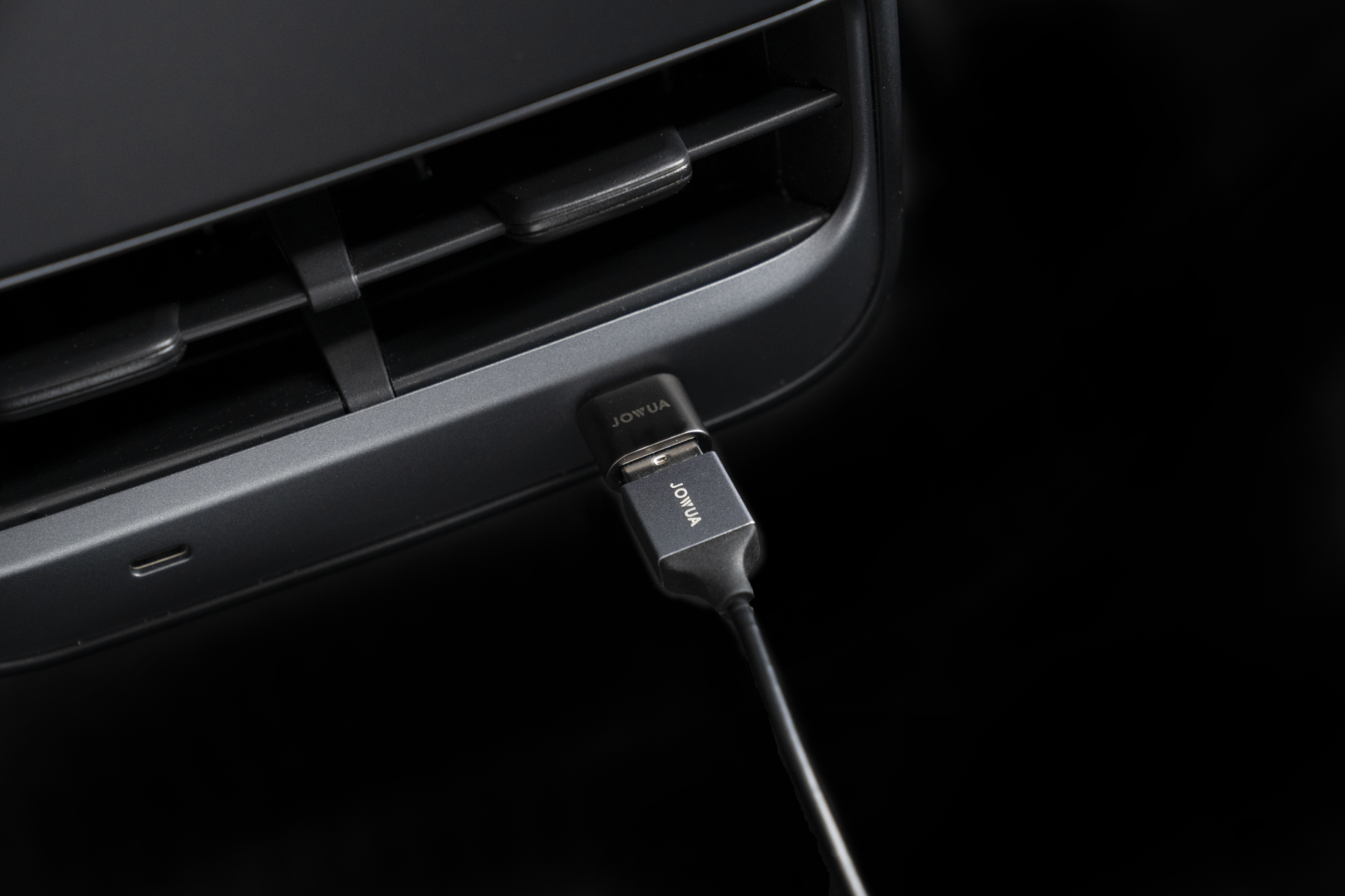 Close-up of a JOWUA USB-C to USB-A Adapter (Data OTG) connected to a USB port on a dark-colored device, with "JOWUA" visible on the plug. The surrounding area suggests it's part of an electronic device or a car dashboard, possibly hinting at TeslaConnect integration.